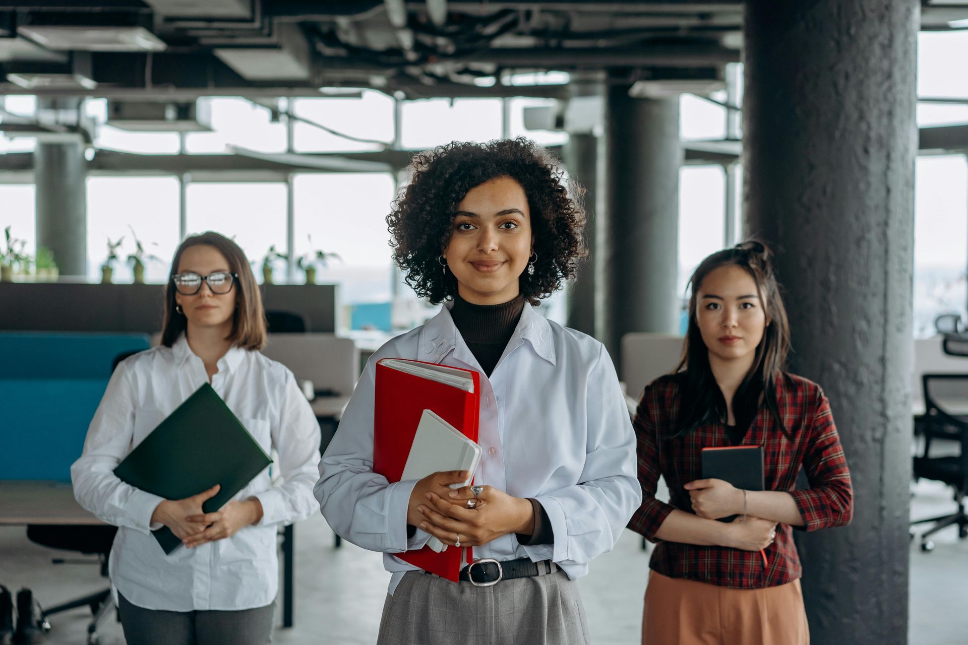 Three HR women in an office setting holding files, smiling at the camera.