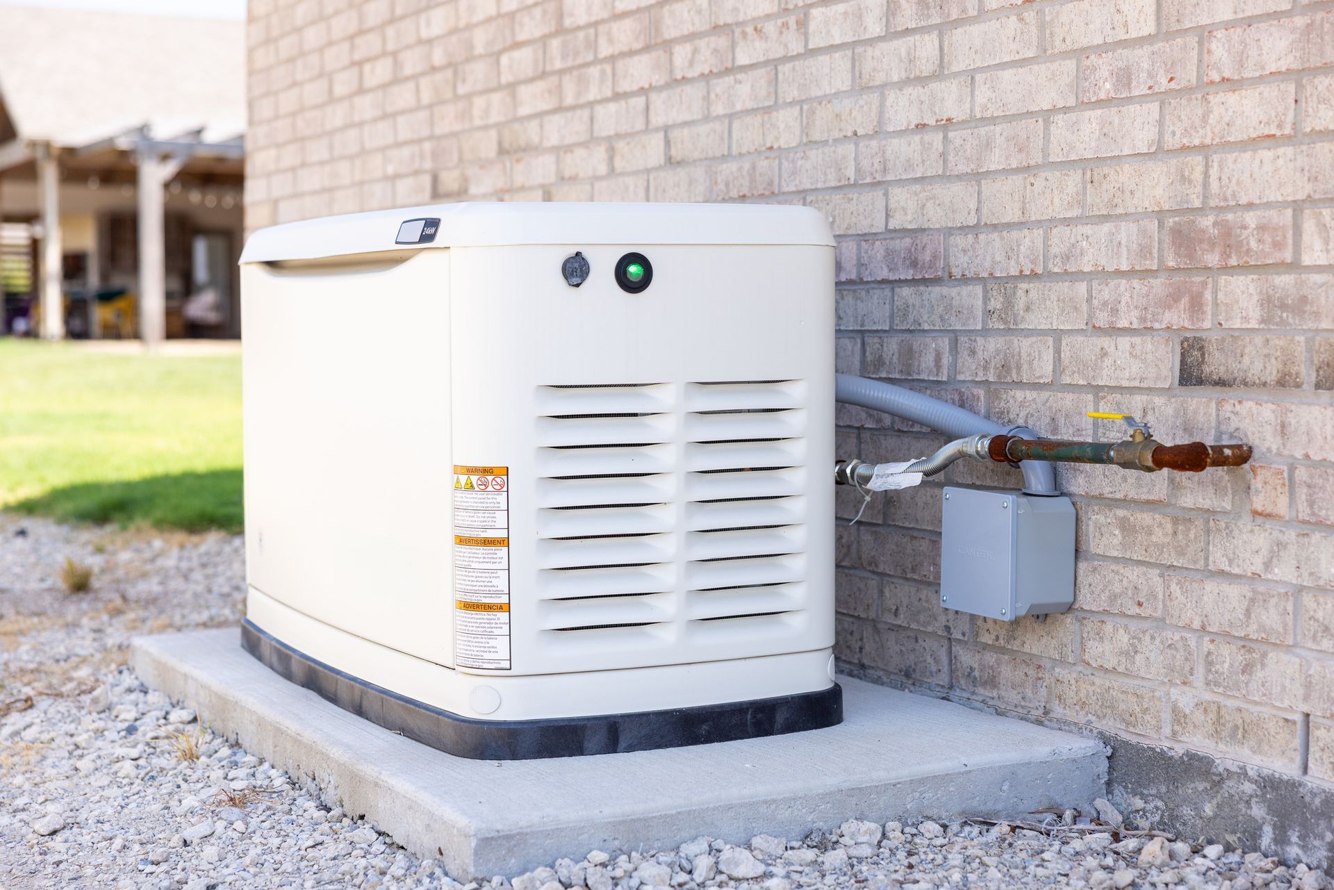 Outdoor air conditioning unit beside a brick house, connected to a gas meter and pipes.