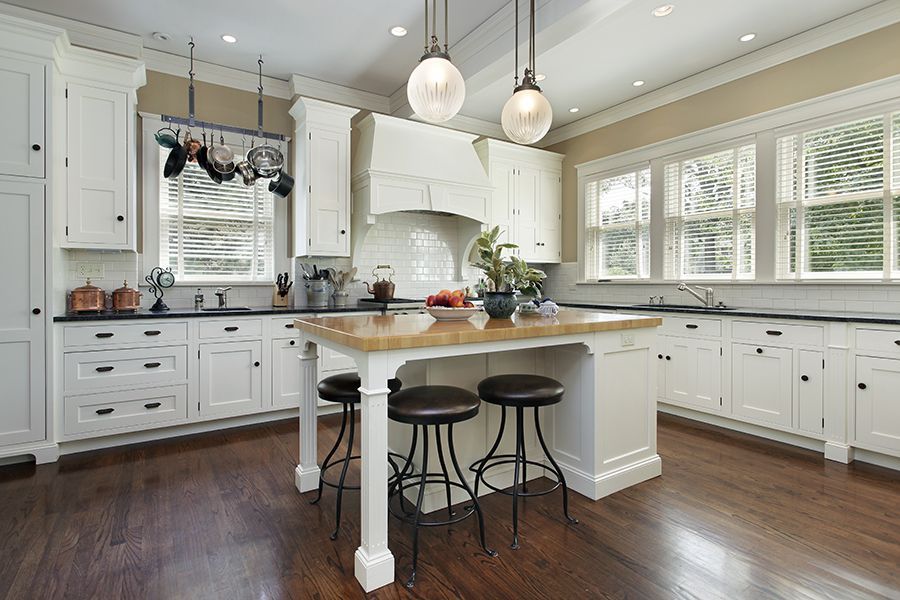 a kitchen with white cabinets , hardwood floors , and a large island .