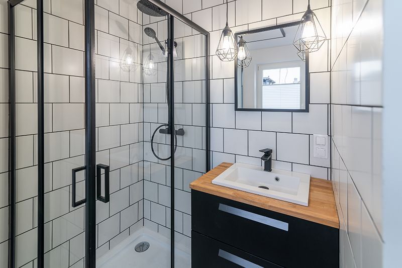 a bathroom with white tiles, a sink, a shower and a mirror.
