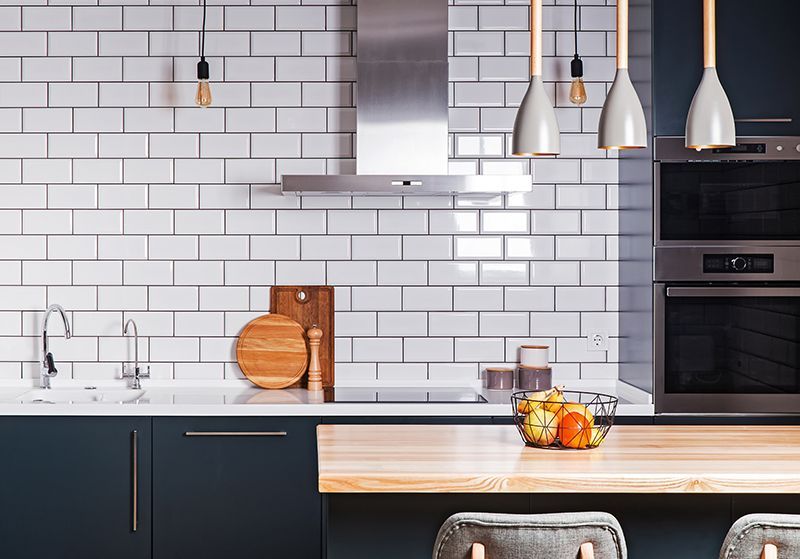 a kitchen with white tiles , stainless steel appliances and a wooden counter top .
