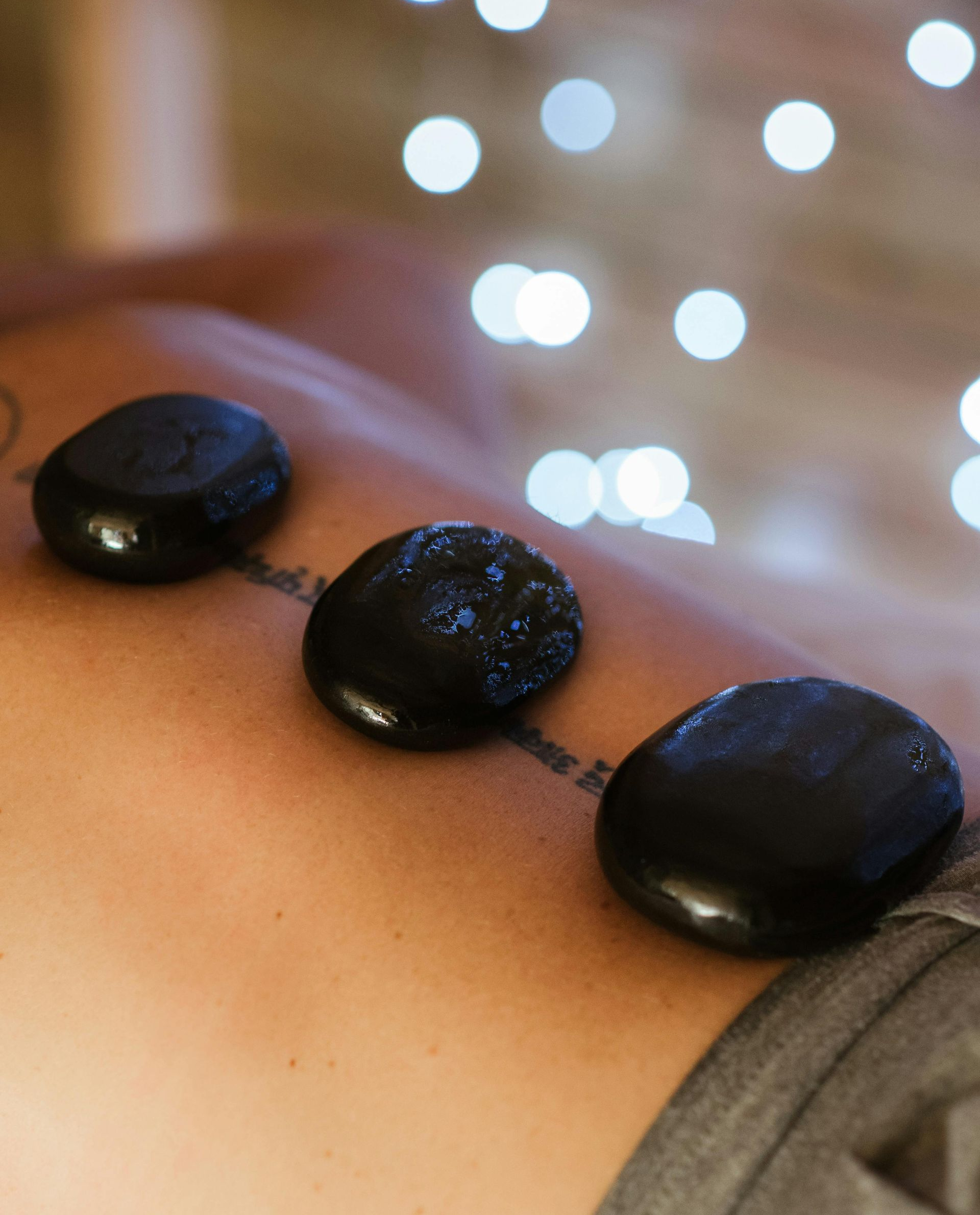 Hot stones on a person's back during a massage, with blurred lights in the background.