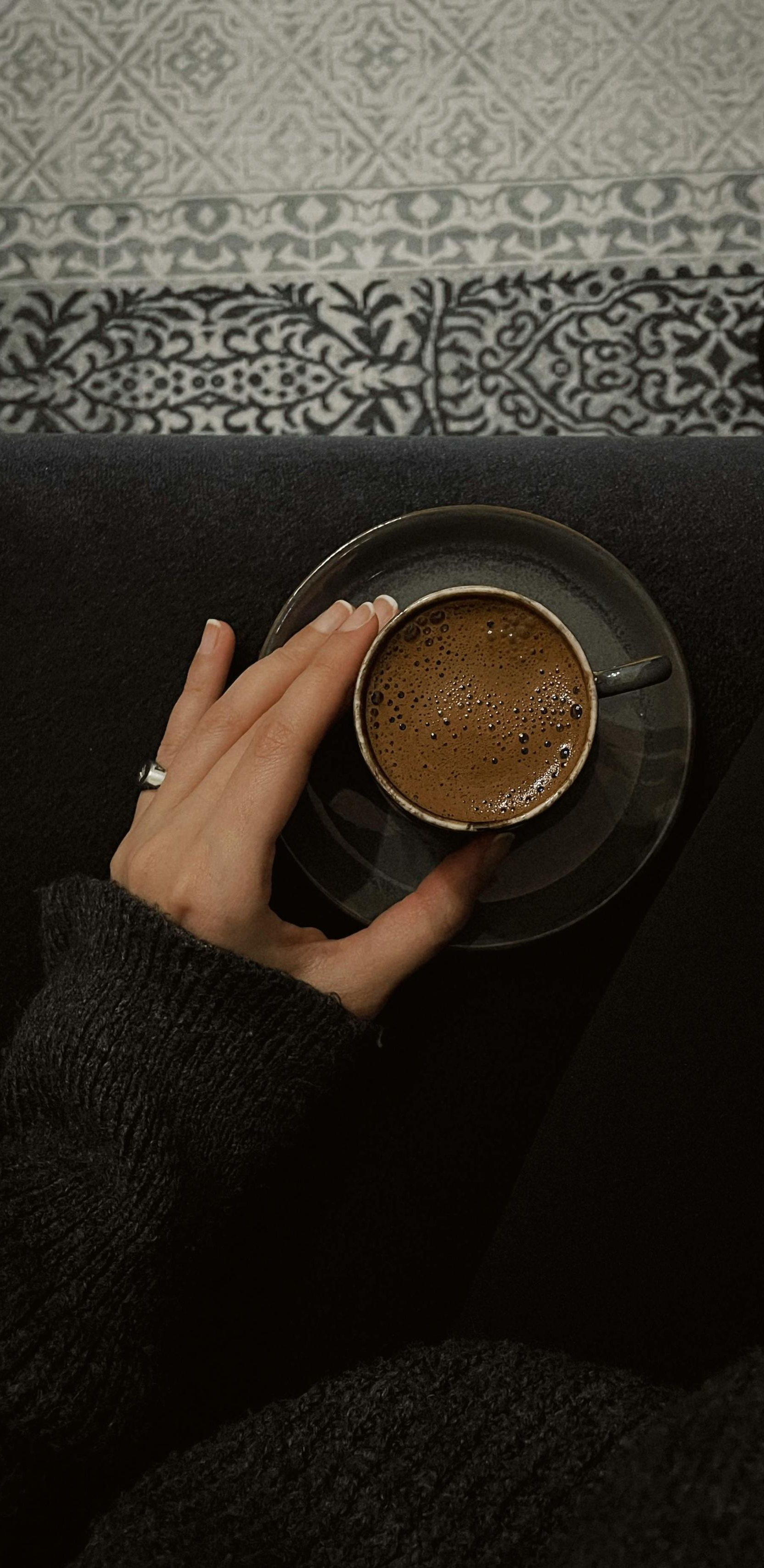 Hand holding a cup of coffee on a saucer, dark setting.