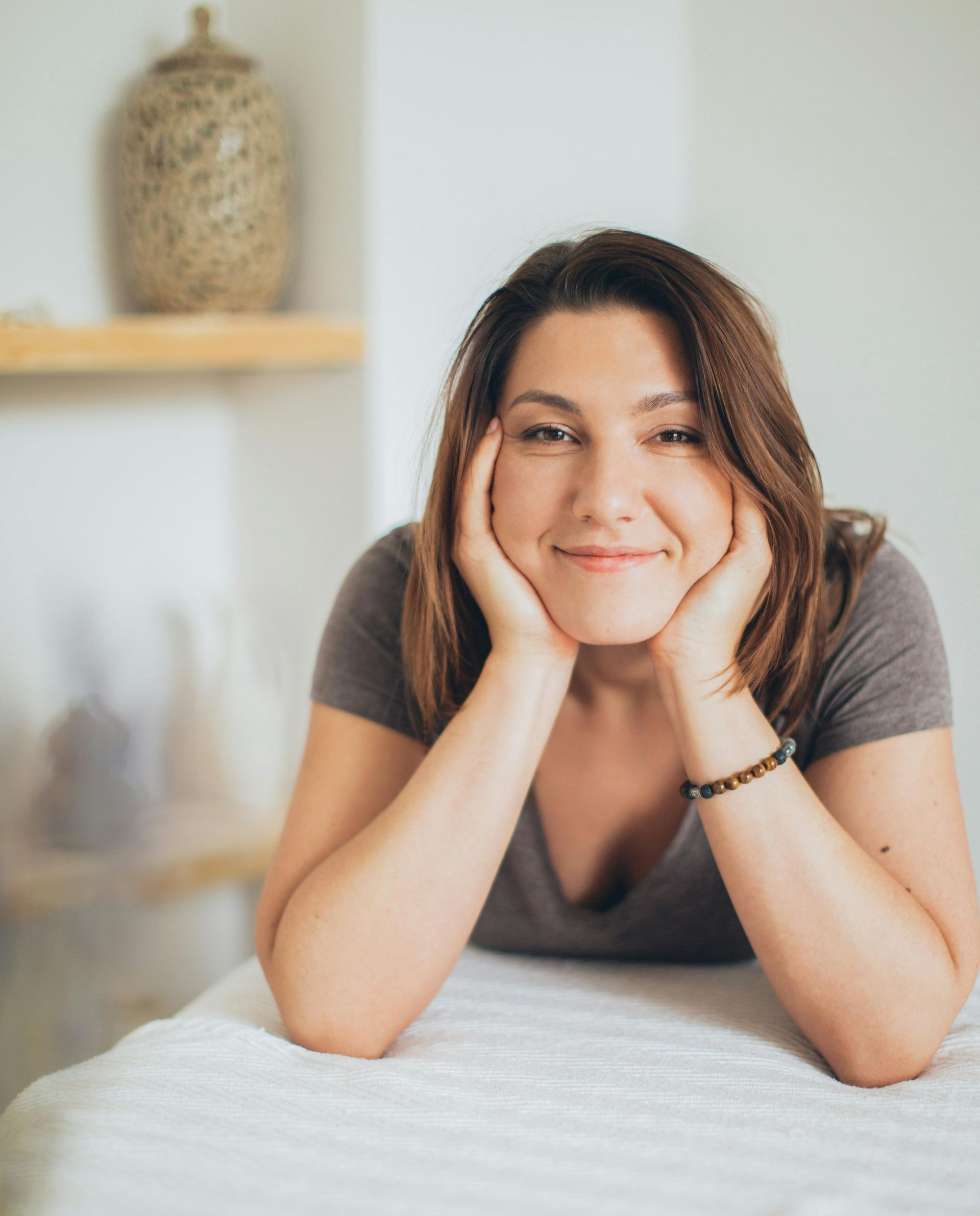 Woman rests face on hands, smiling, in a spa setting.