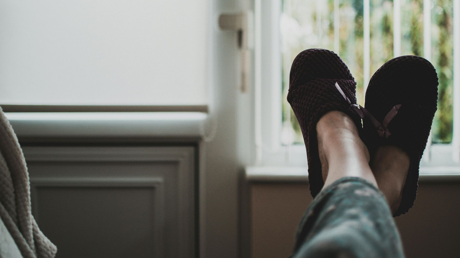 Feet in fuzzy slippers resting by a window, indoors.