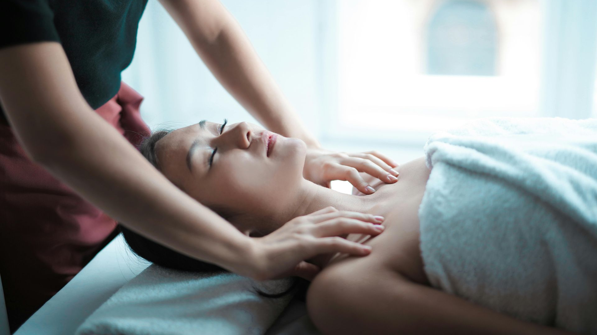 Person receiving a massage on their neck and chest in a bright room.