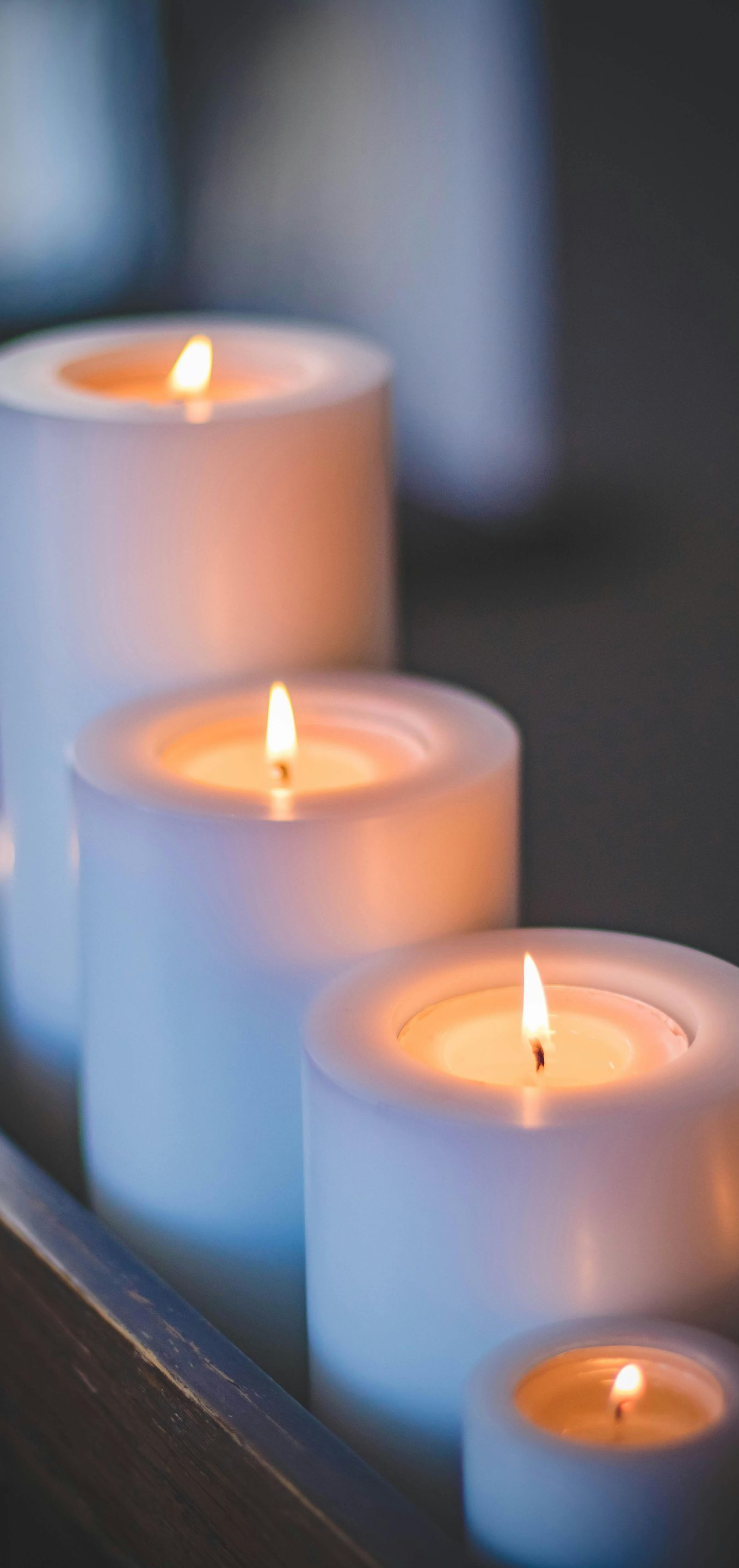 White lit candles of varying sizes, warm glow, soft focus.