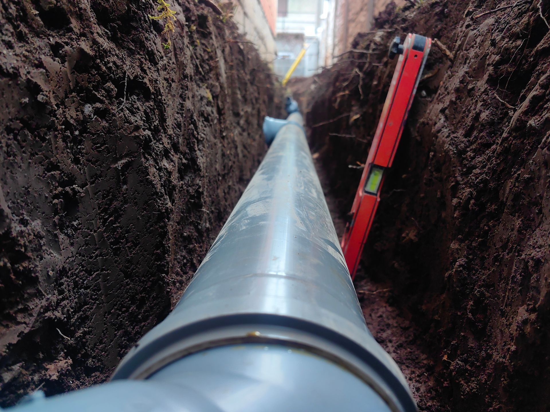 A new water main pipe was laid at the bottom of a deep excavation trench with a red leveling tool