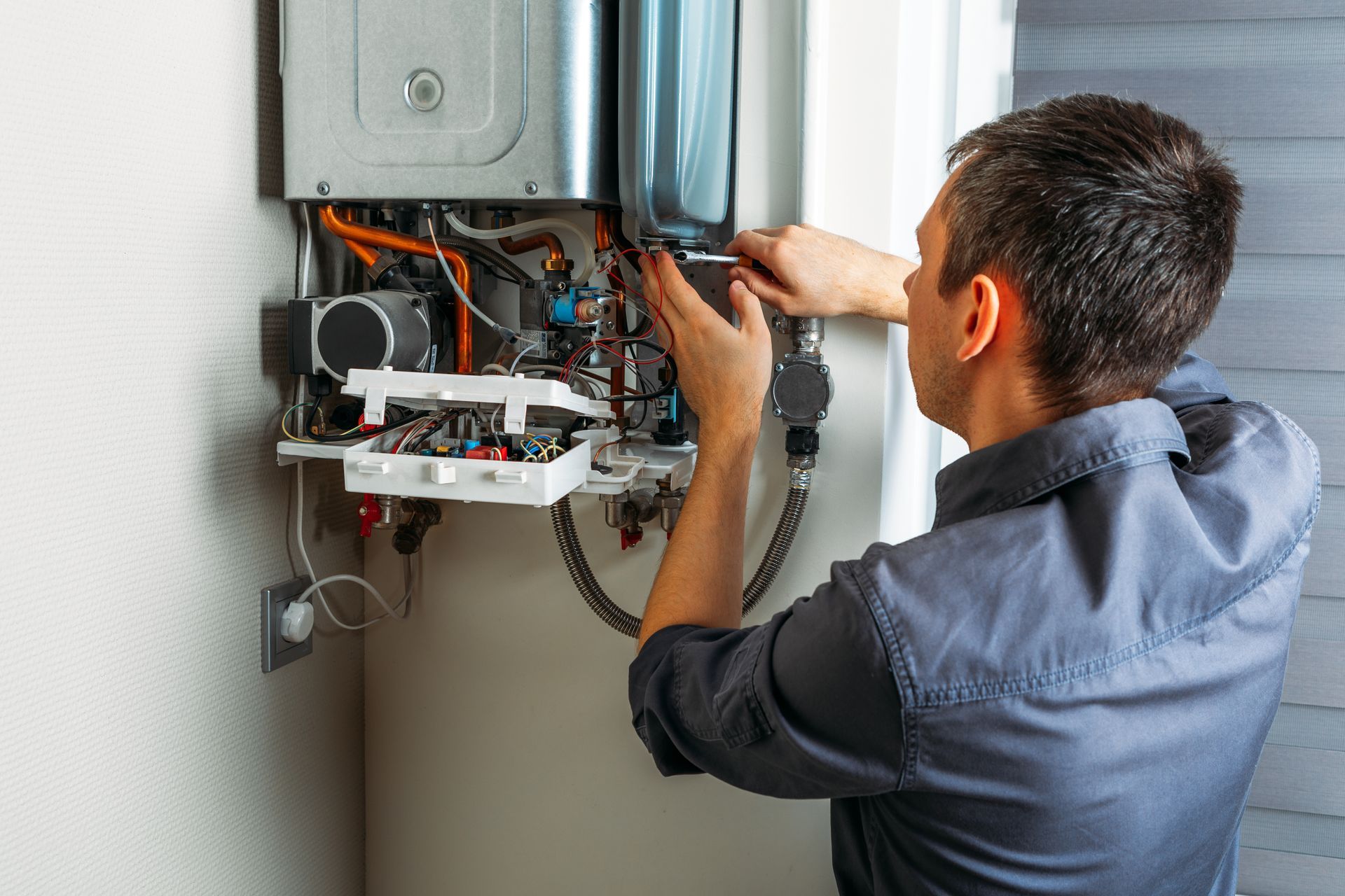 A plumber servicing an open internal wiring and valves of a wall-mounted tankless water heater unit