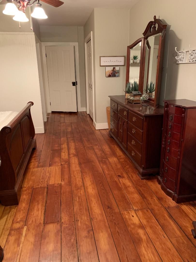 A bedroom with hardwood floors a dresser and a mirror