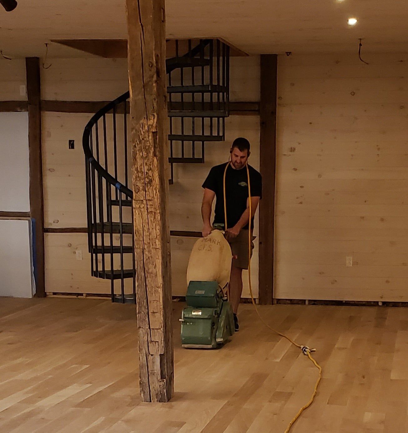 A man sanding a wooden floor next to a spiral staircase