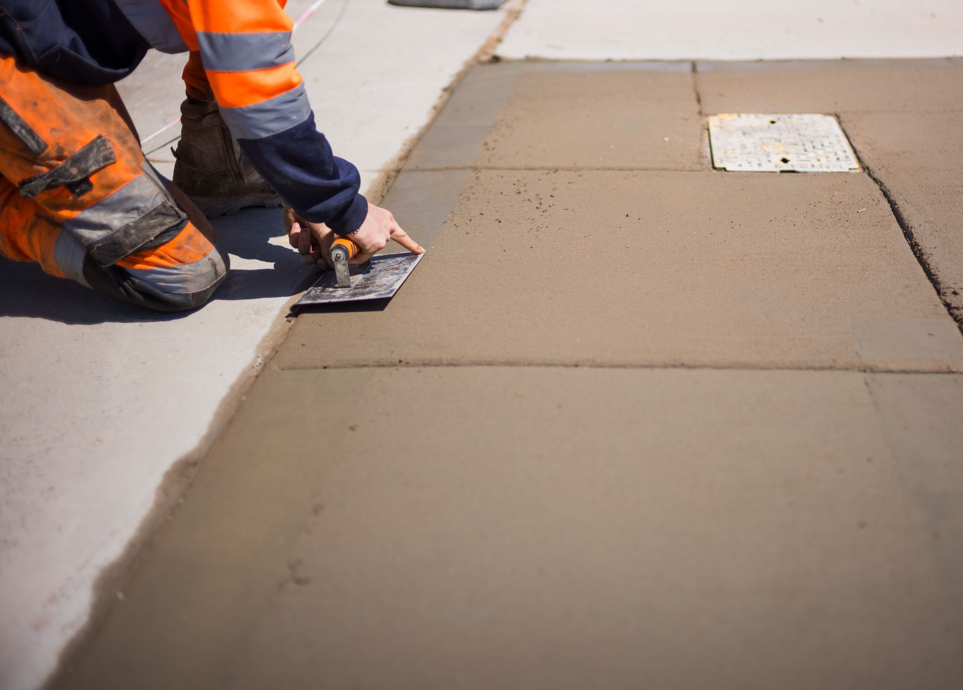 Worker smoothing wet concrete with a hand trowel during a slab repair.