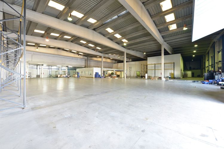 A wide-angle interior view of a large, empty industrial warehouse with high ceilings, exposed beams, and concrete floors. A wide-angle interior view of a large, empty industrial warehouse with high ceilings, exposed beams, and concrete floors.