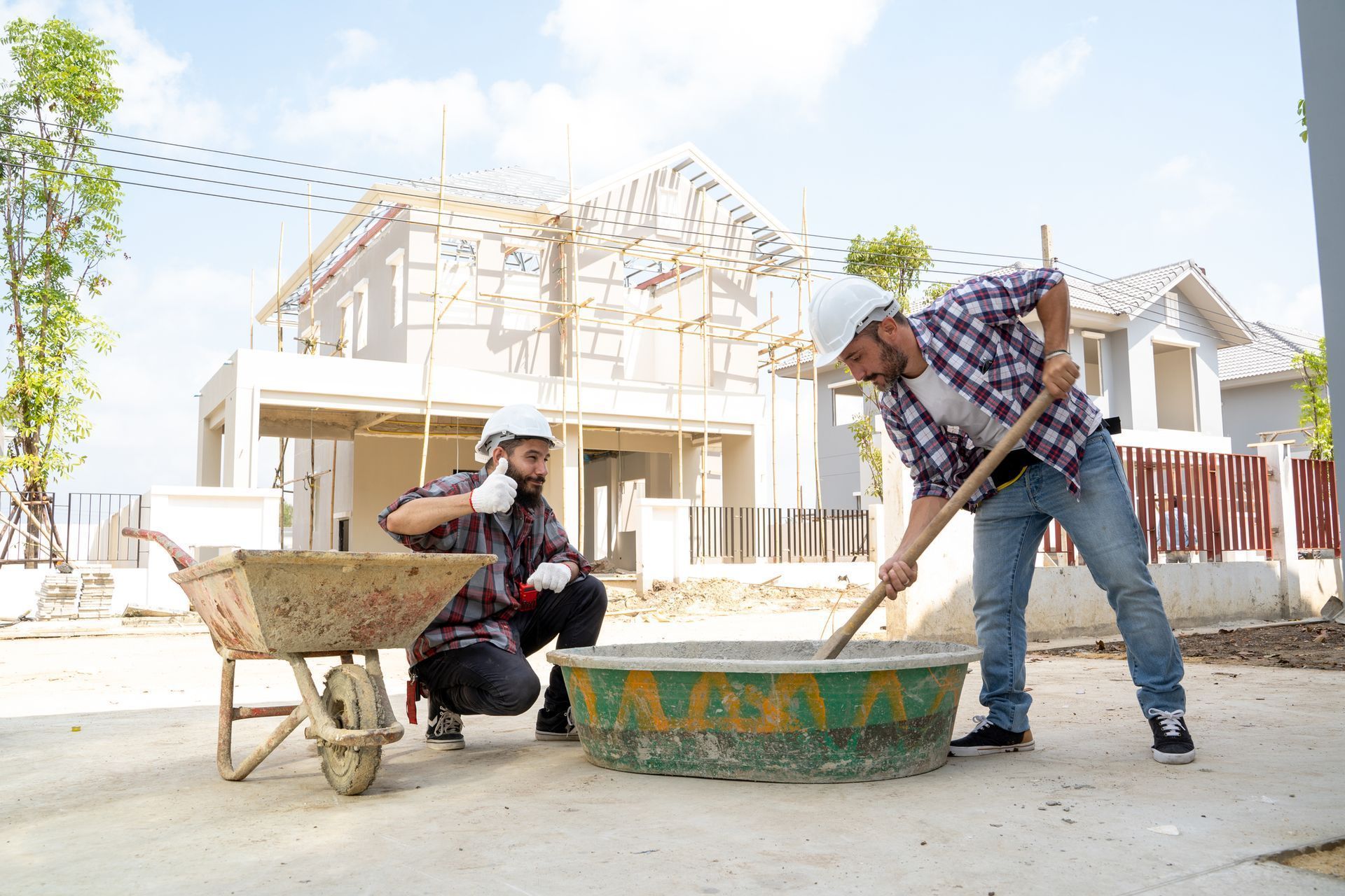 A concrete contractor holds a thumbs up while another is mixing cement at a residential construction site. A concrete contractor holds a thumbs up while another is mixing cement at a residential construction site.
