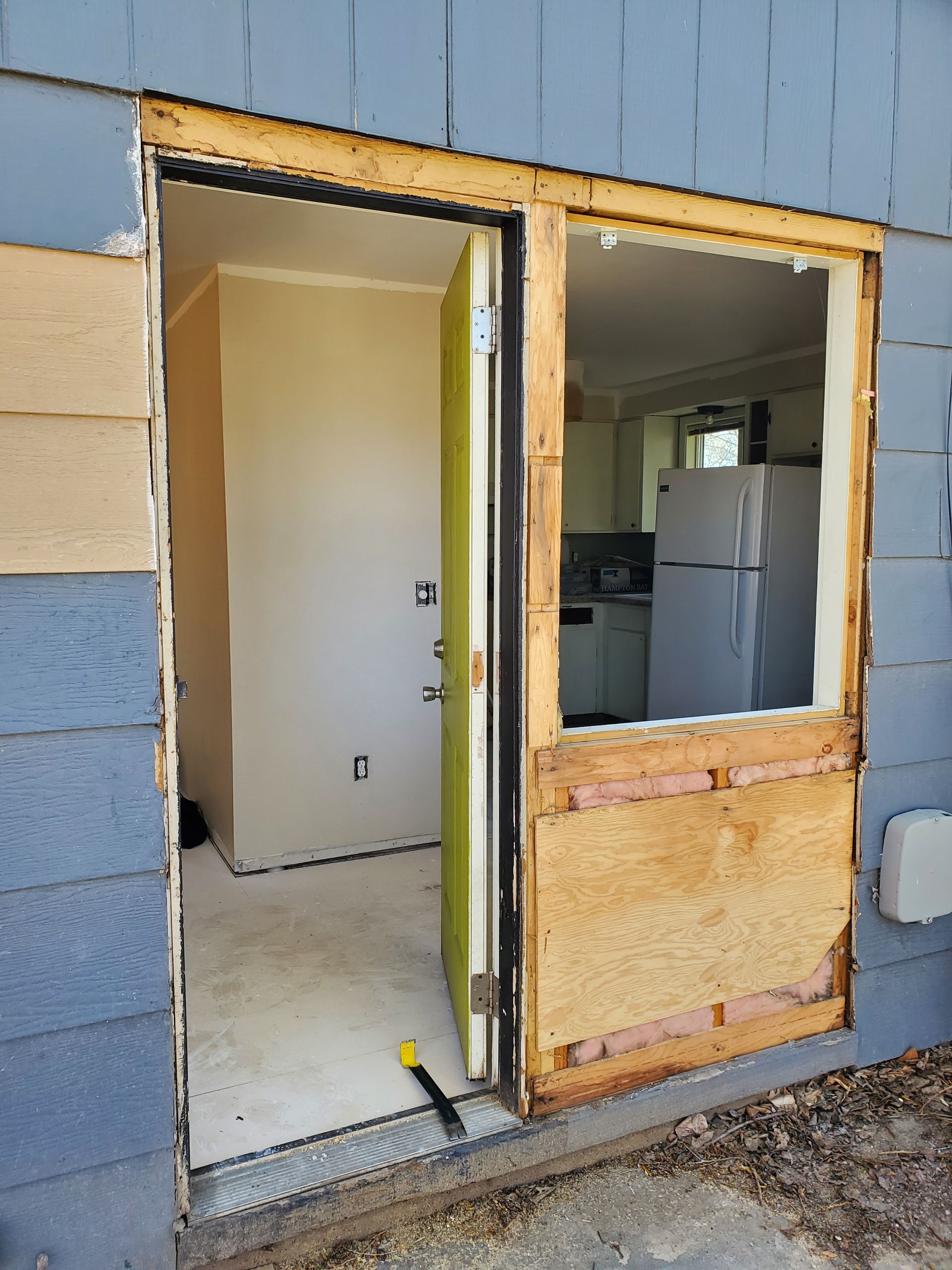 Partially open doorway in a blue exterior wall, showing a white room and a kitchen inside.