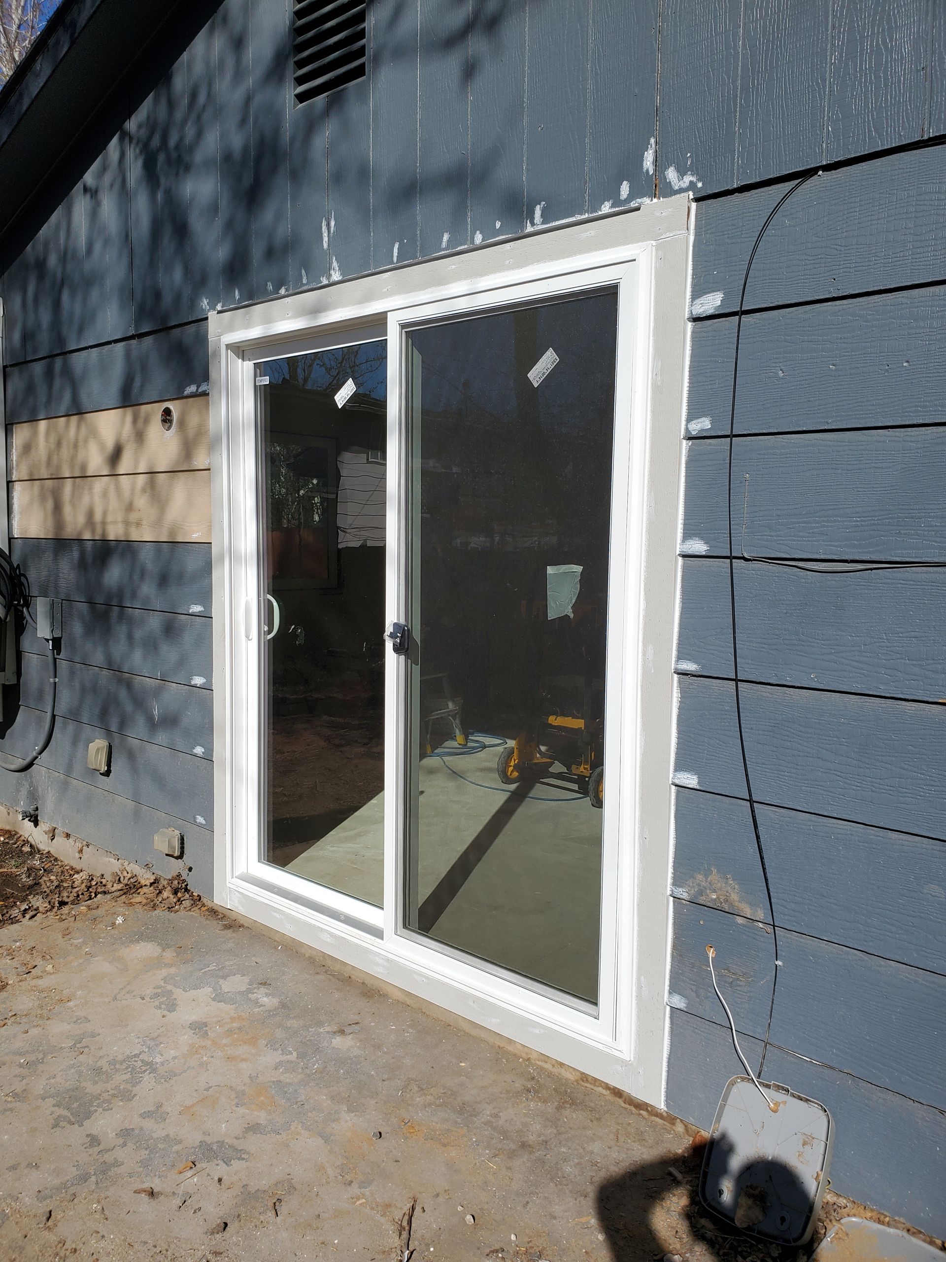 Sliding glass patio door in a white frame on a blue-sided exterior wall.