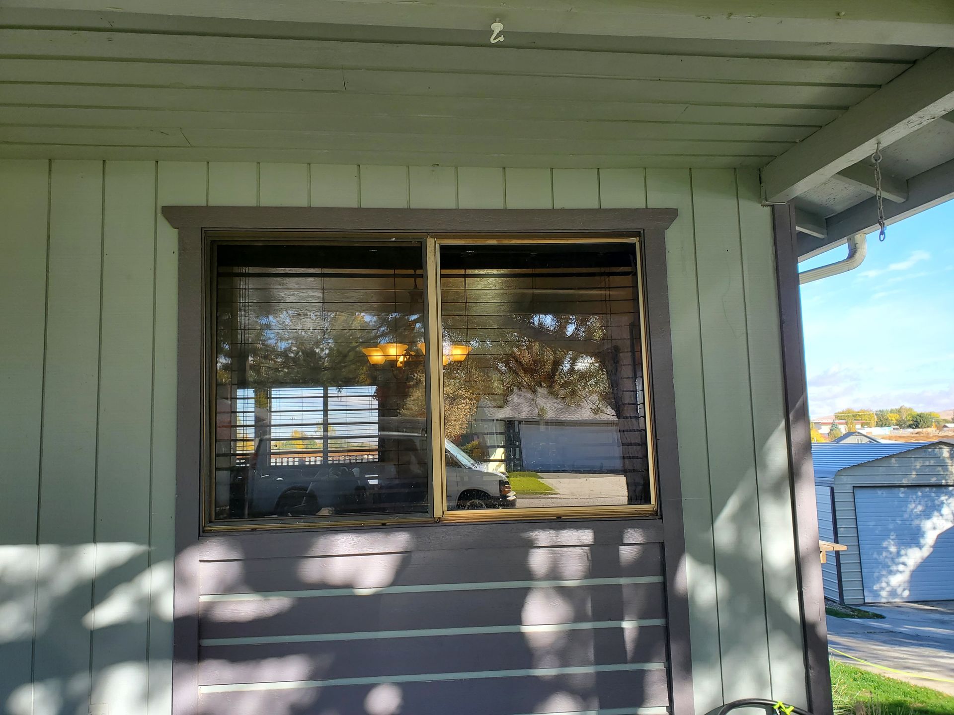 Window on a white-sided porch overlooking water, with sunlight and tree shadows.