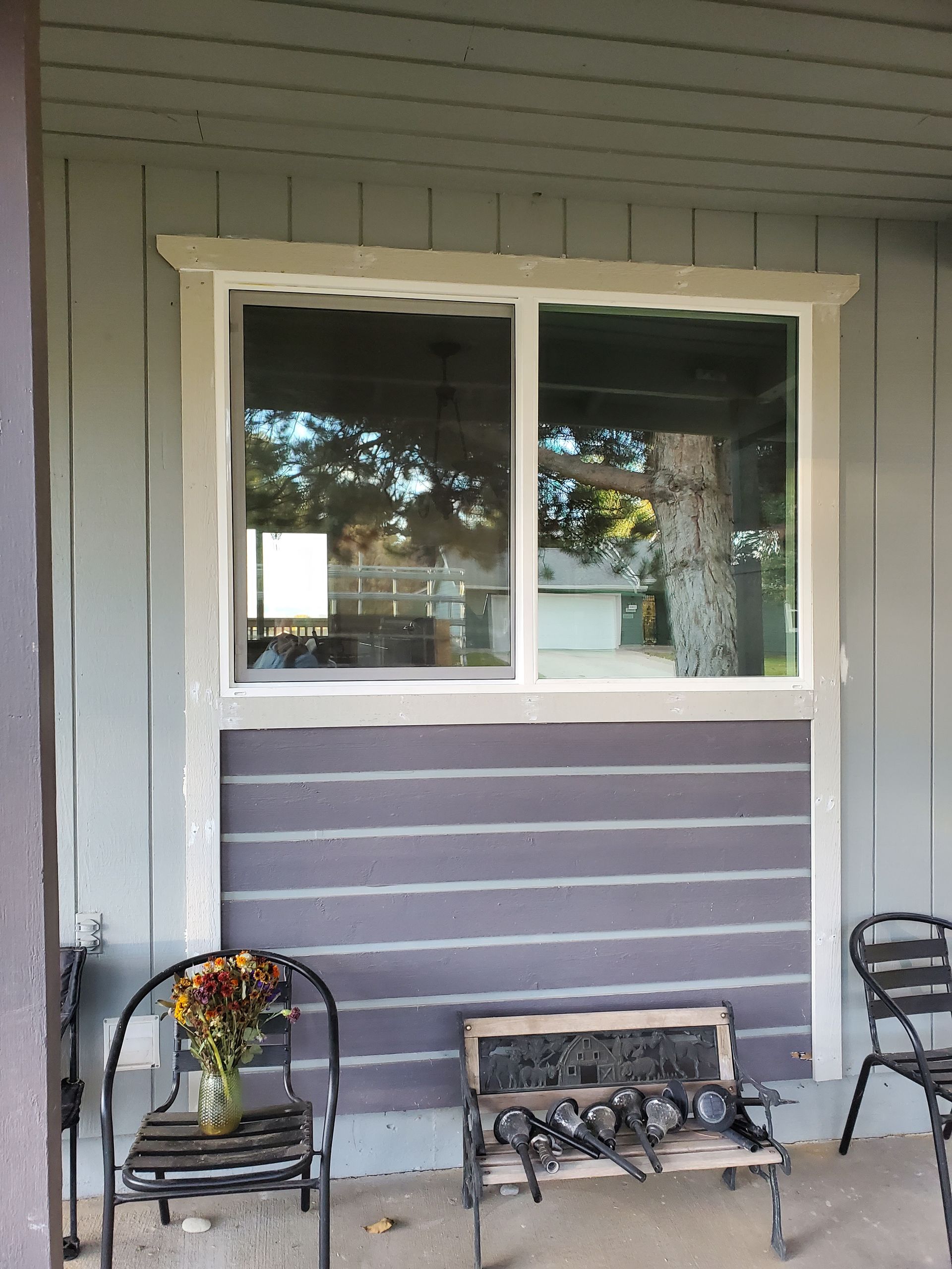 Front porch with a window above a purple siding panel, flanked by metal chairs and a small bench.