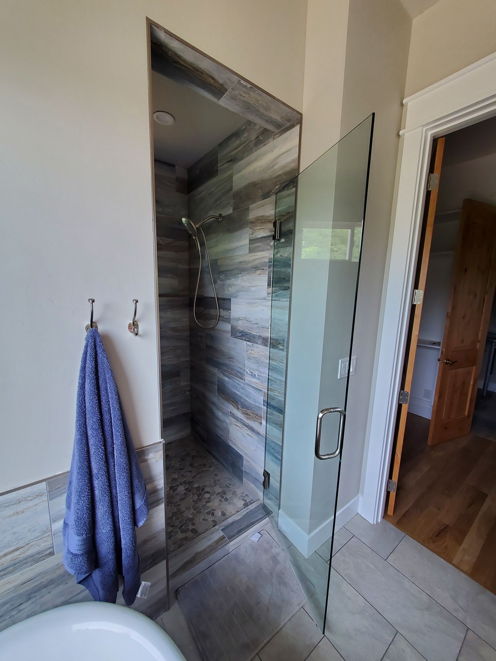 Bathroom with glass shower door, striped tiled shower wall, and blue towel on a hook