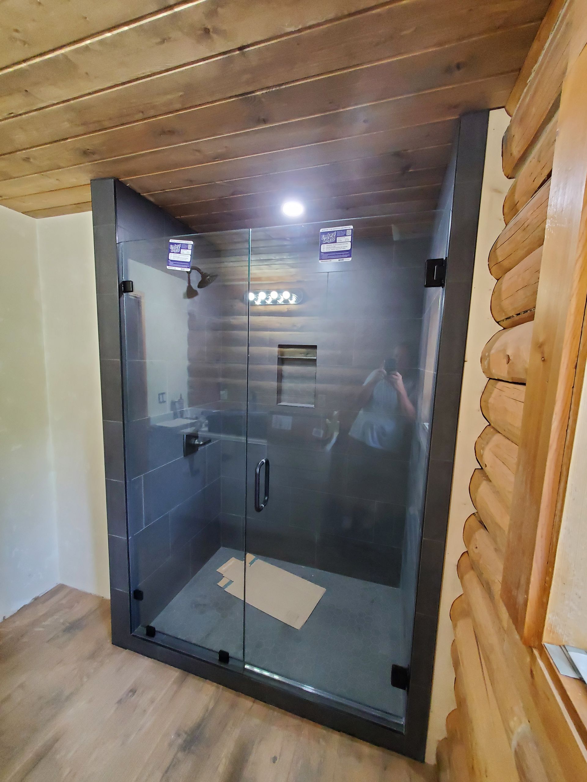 Glass shower enclosure in a log cabin bathroom with wood walls and ceiling