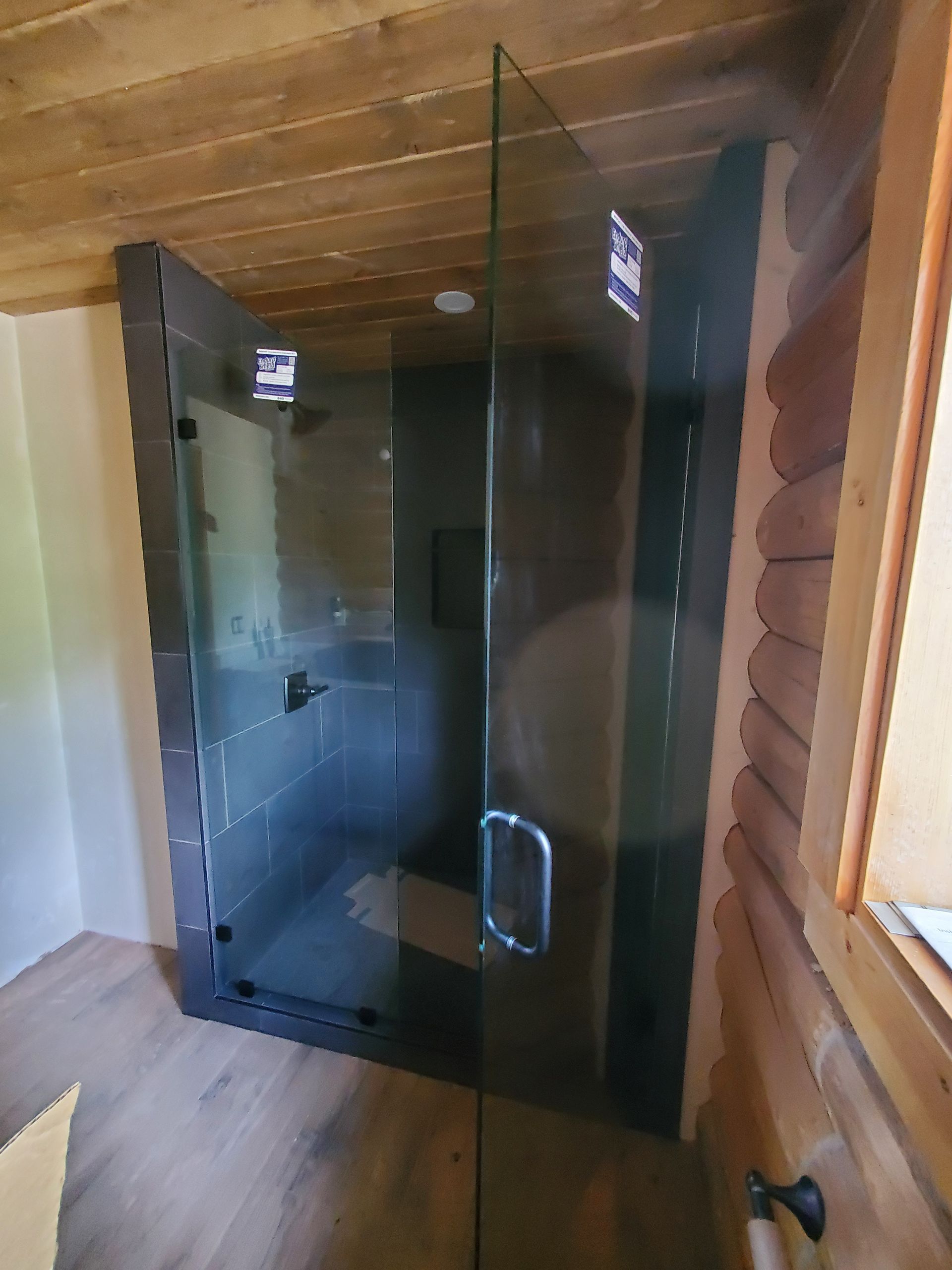 Glass-door shower in a wooden sauna room, with dark tinted panels and a metal handle.