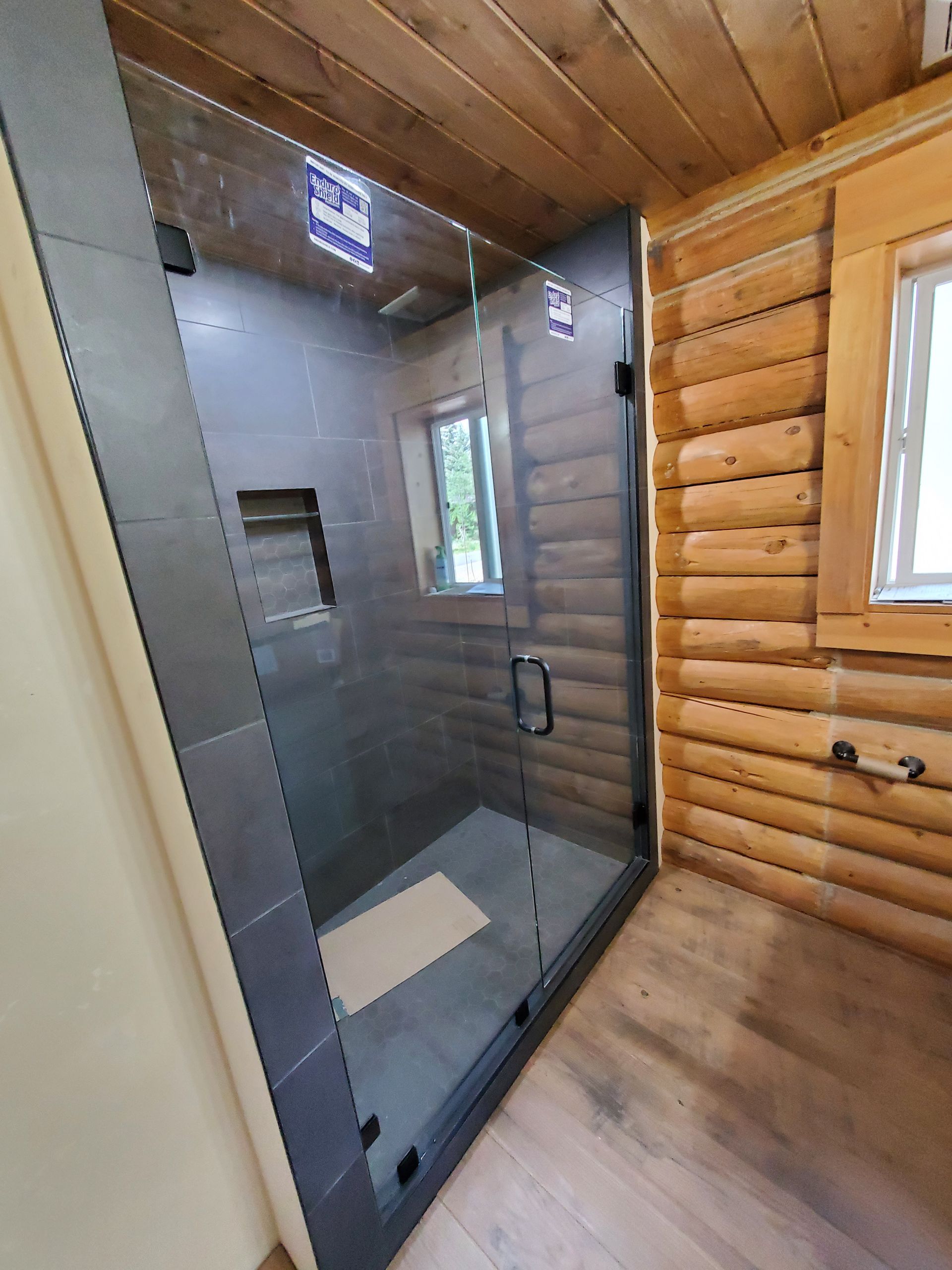 Modern bathroom with a glass-enclosed shower, log-style wood walls, and a small window.