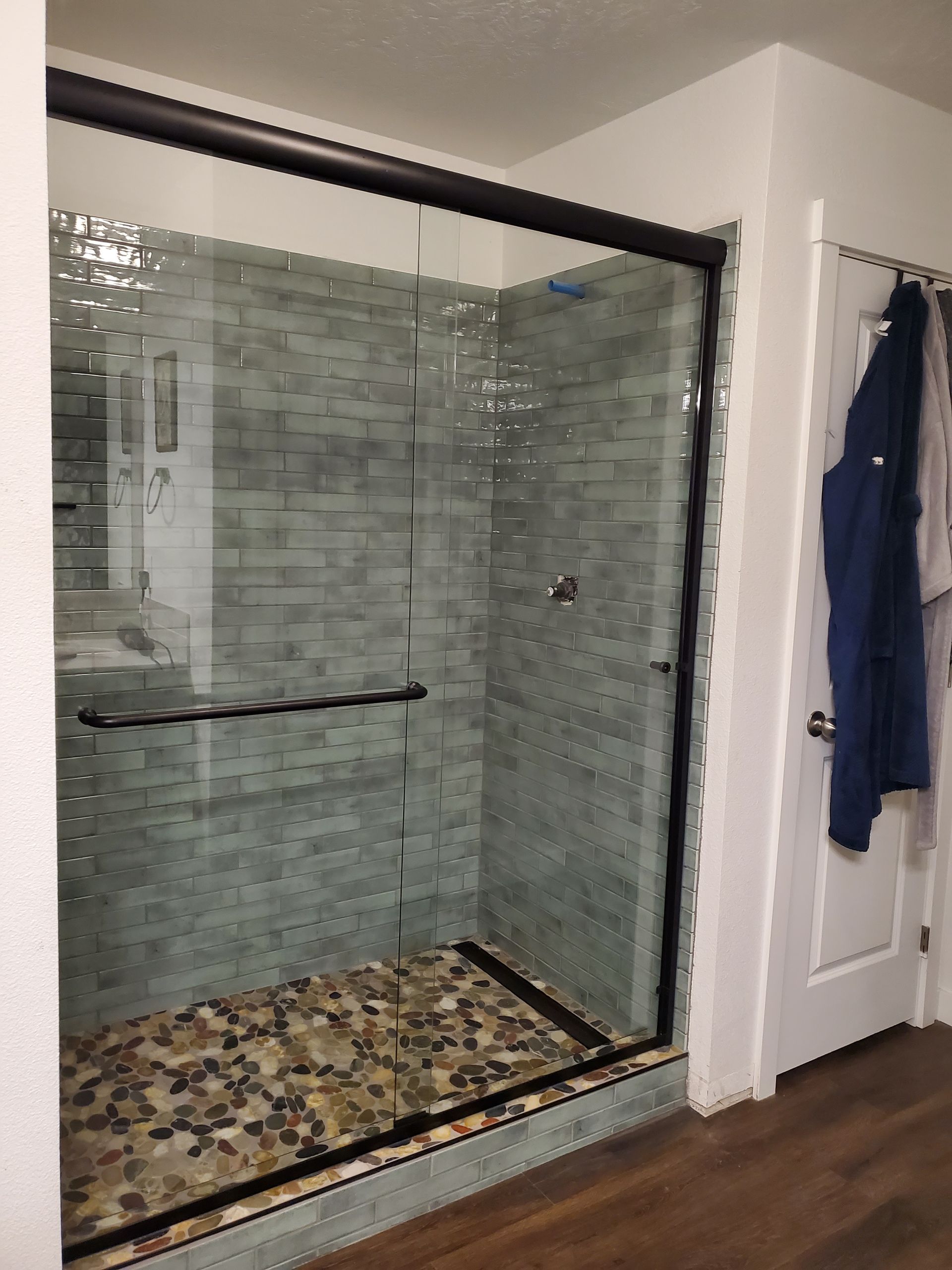 Glass shower enclosure with gray tile walls and pebble-floor base in a bathroom