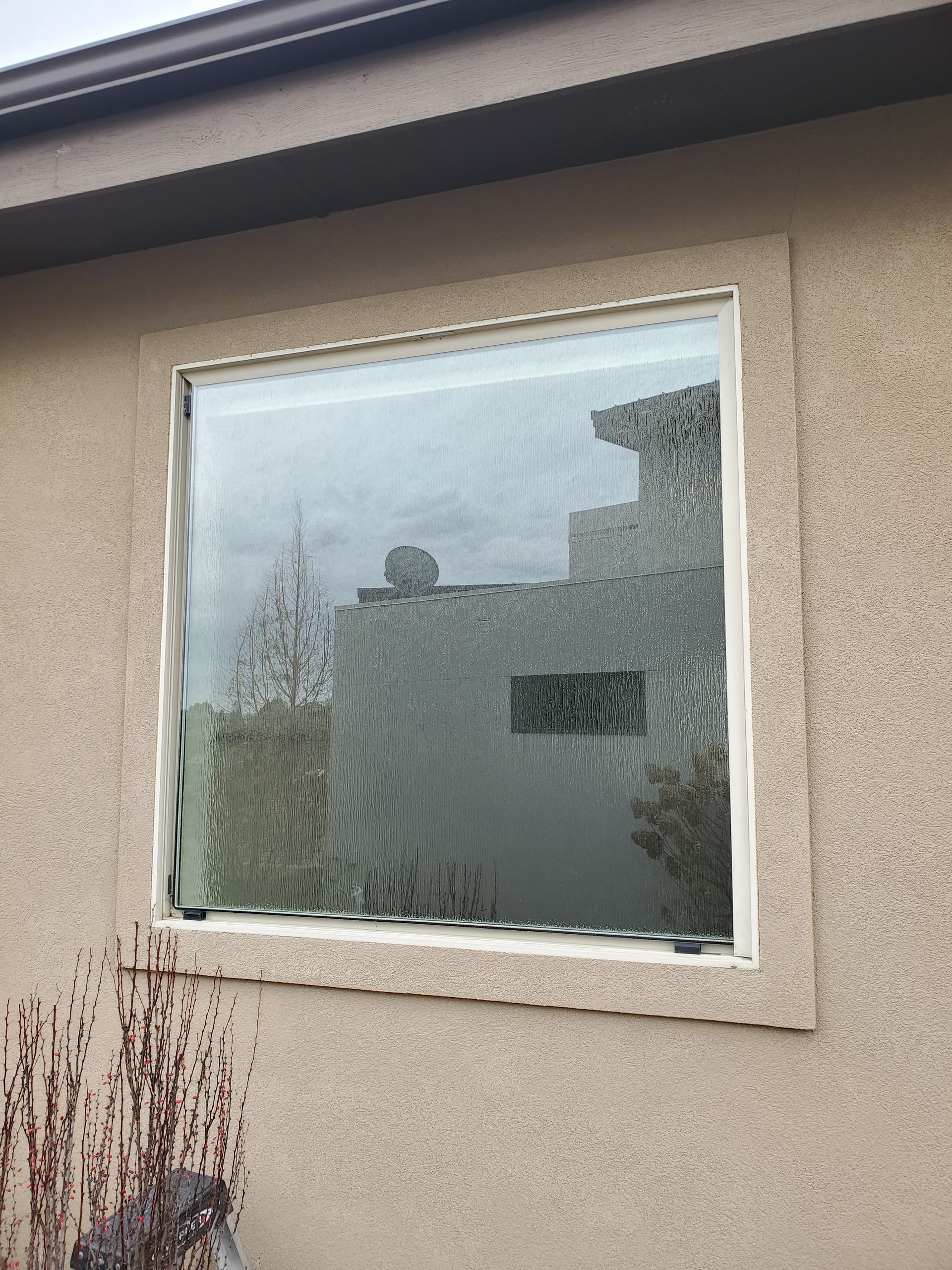 Fogged window in a beige stucco wall with a white frame and house reflections.