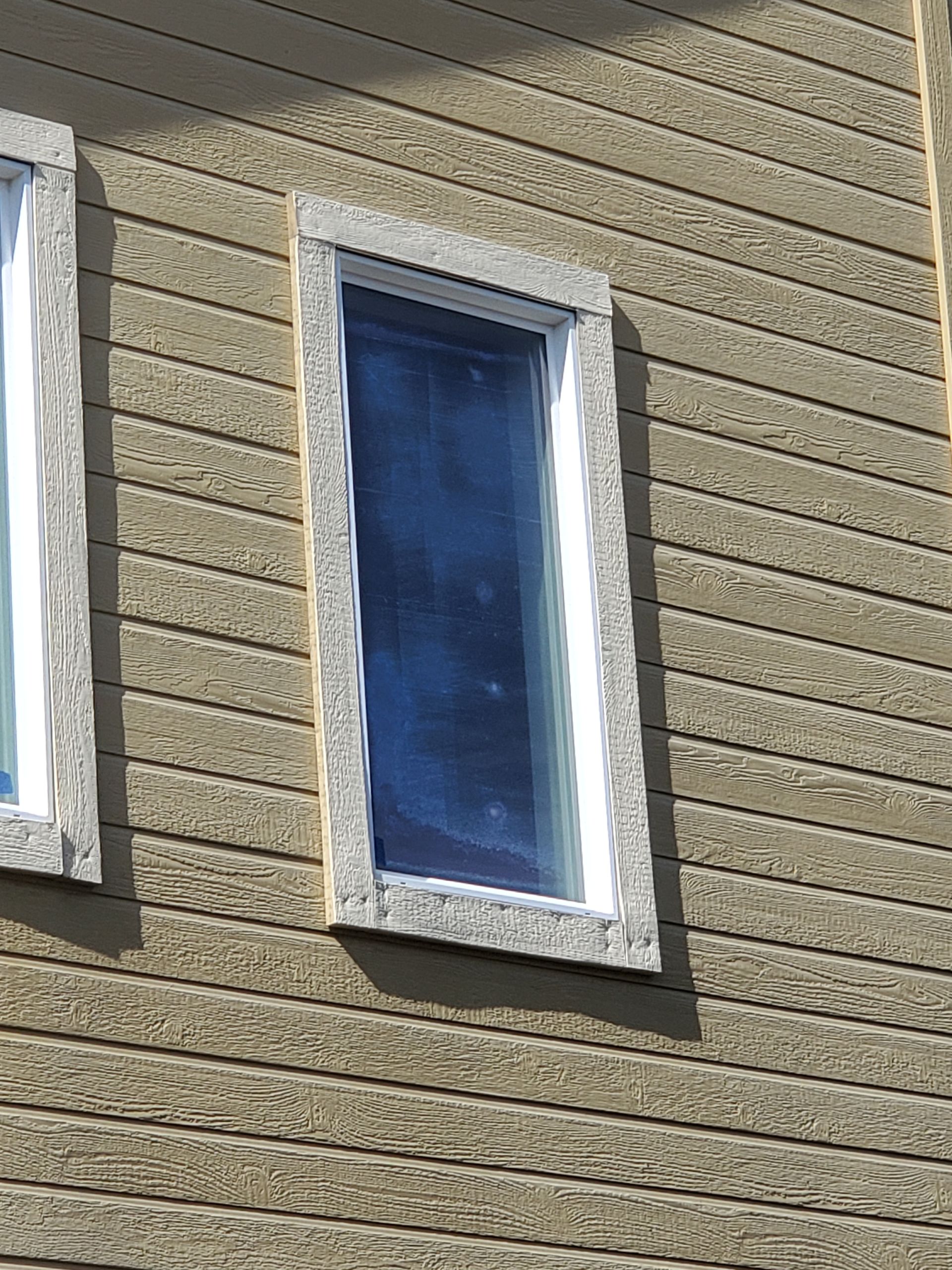 Two narrow windows with white trim on a beige stucco building wall