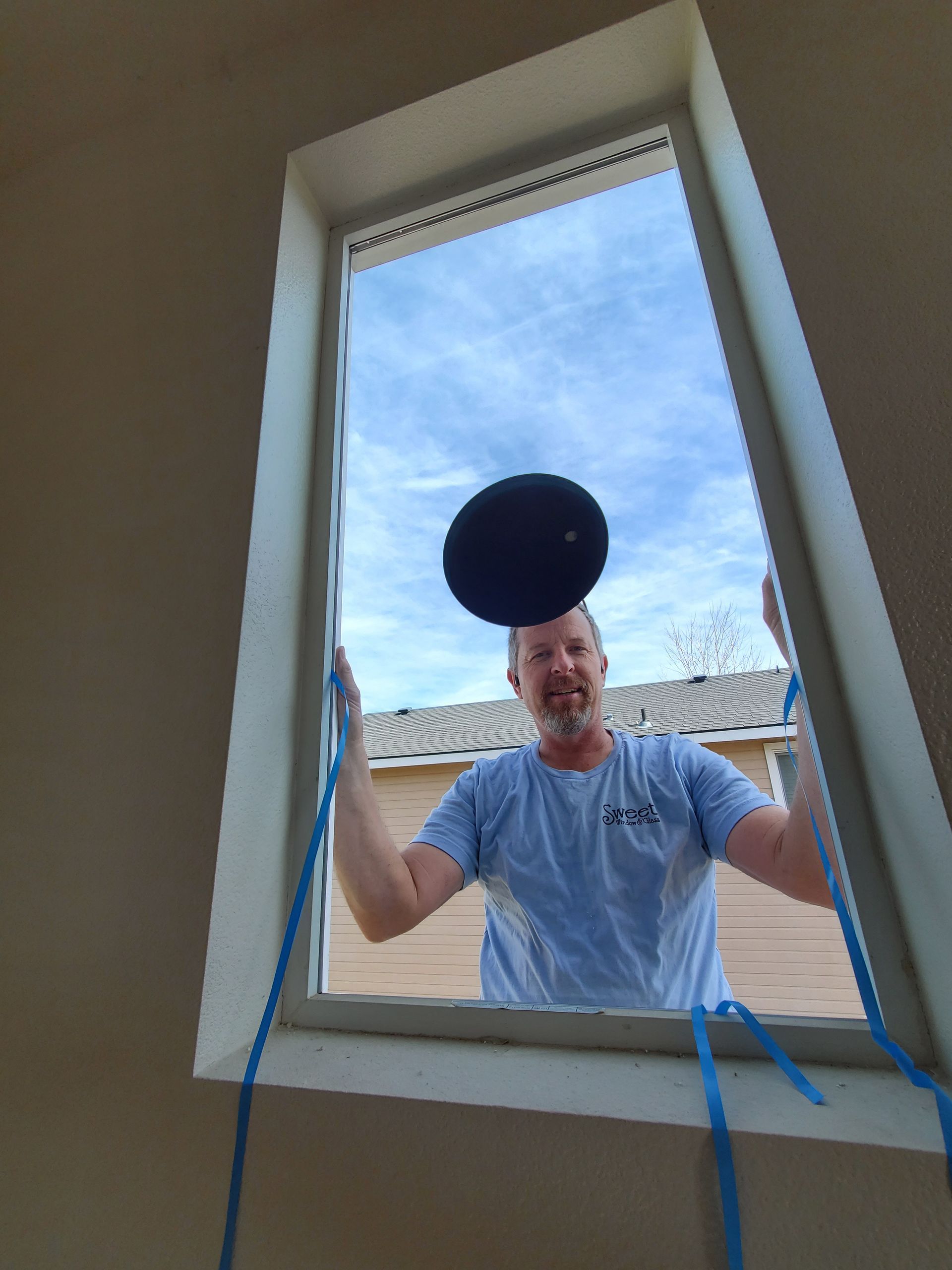 Man standing outside a window, looking in, with a black circular object above him and blue cords on the sill