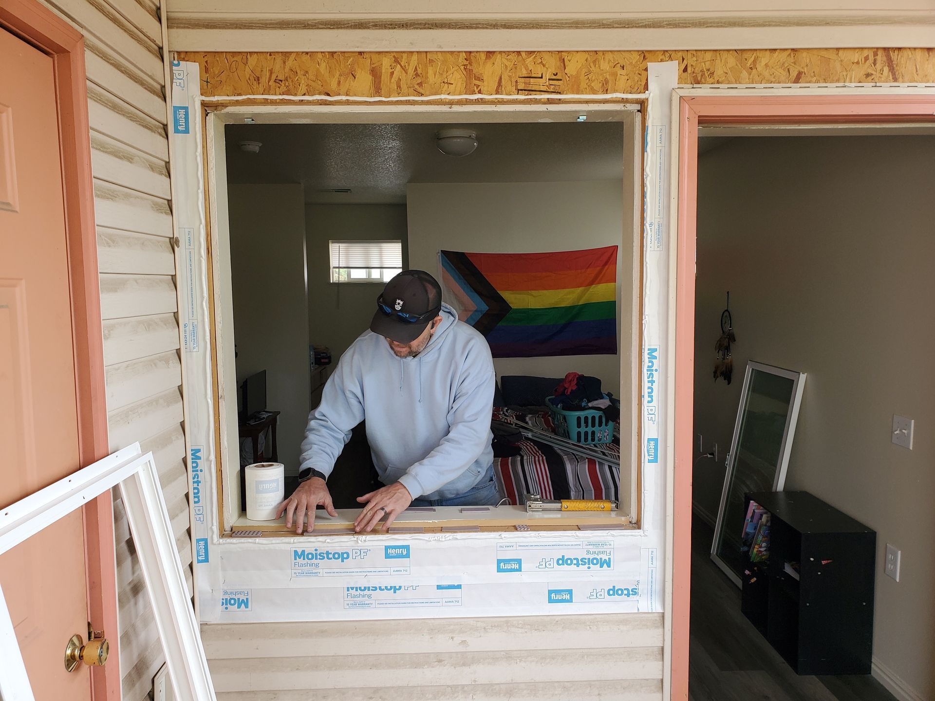 Person working at an open window frame during home renovation, with a rainbow flag inside.