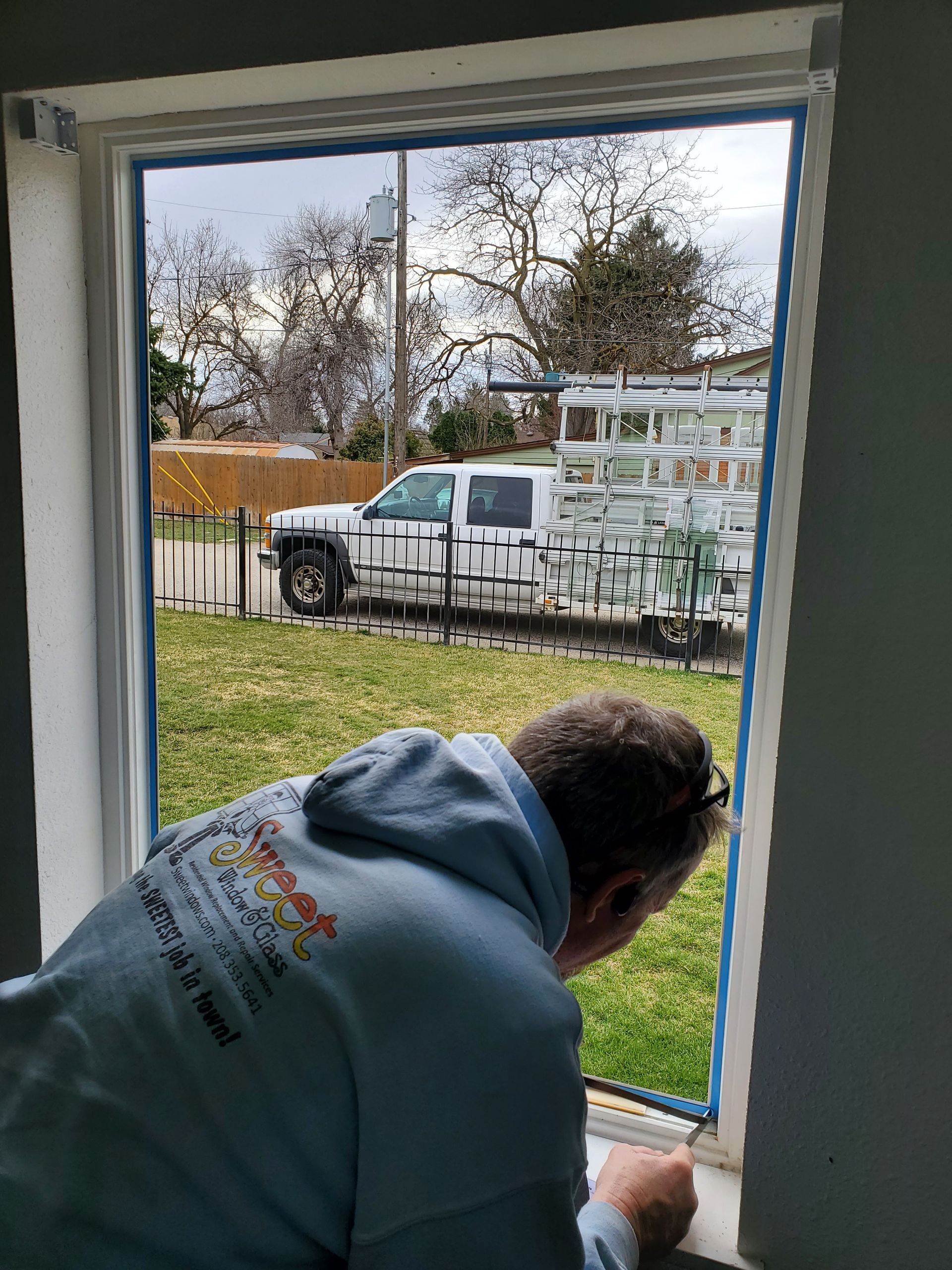 Person leaning out an open window toward a white utility truck parked on a grassy yard.