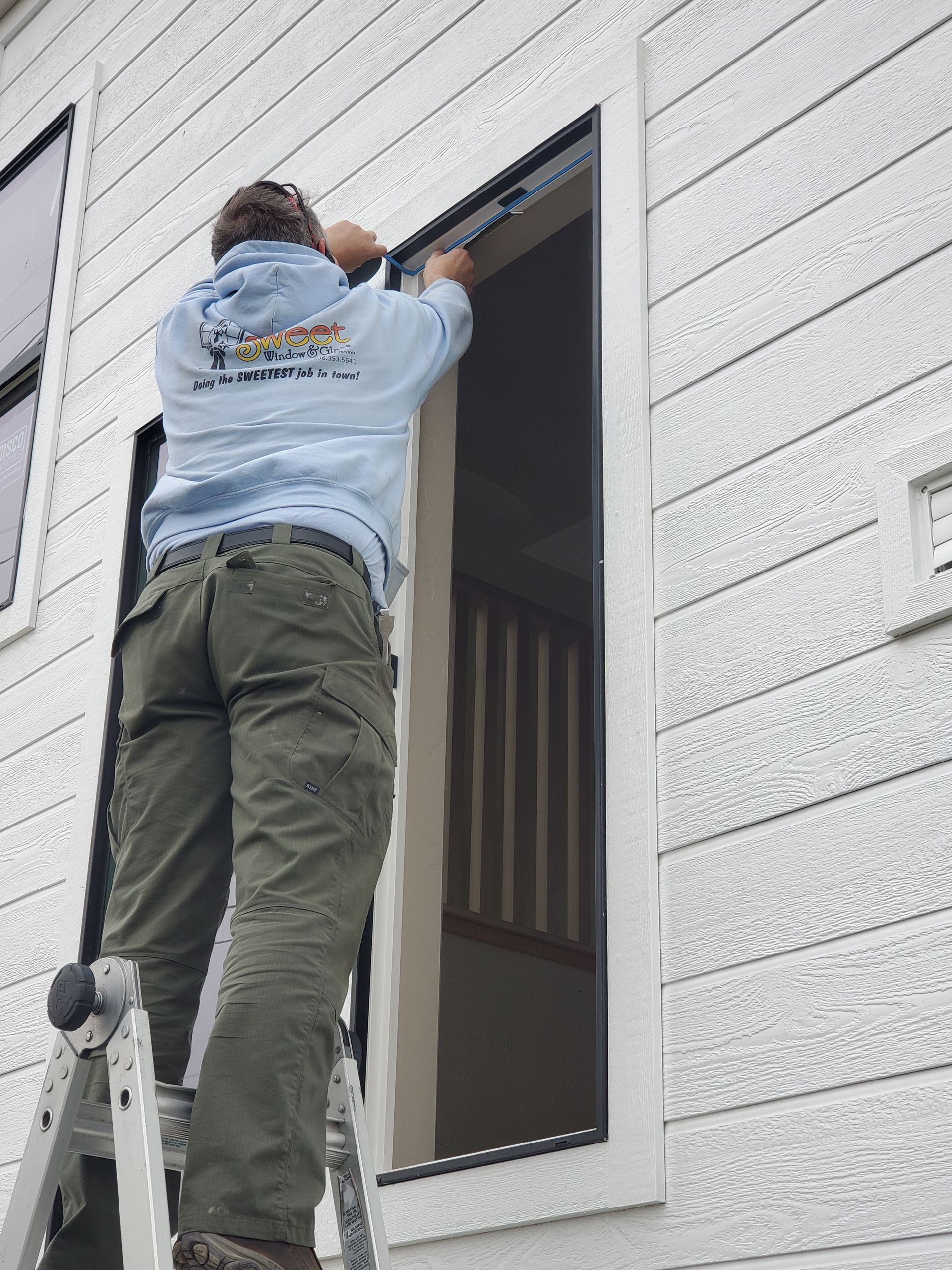 Person on a ladder installing a window frame on a white house exterior