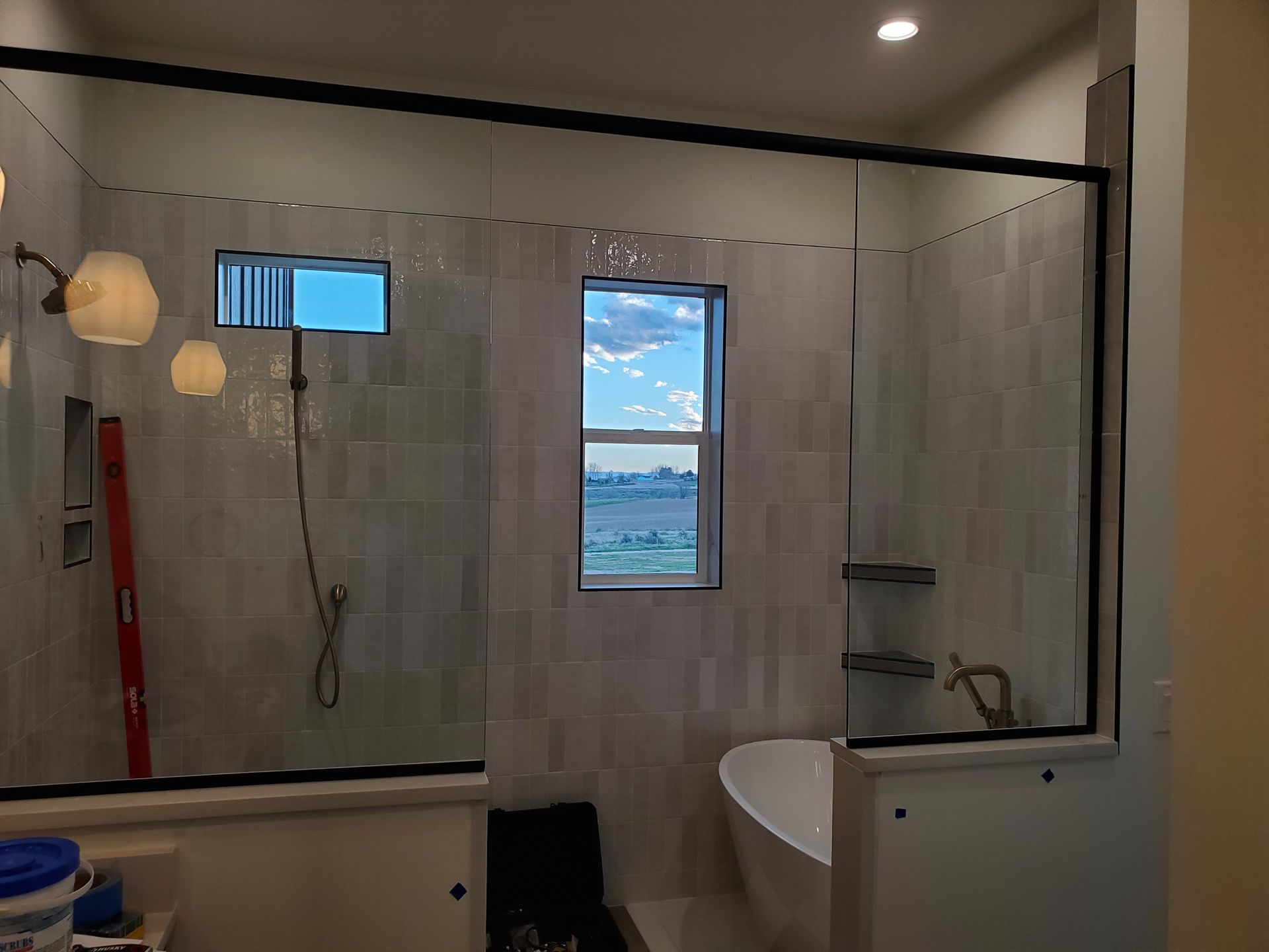 Modern bathroom with glass shower, window, and white tub under warm ceiling lights