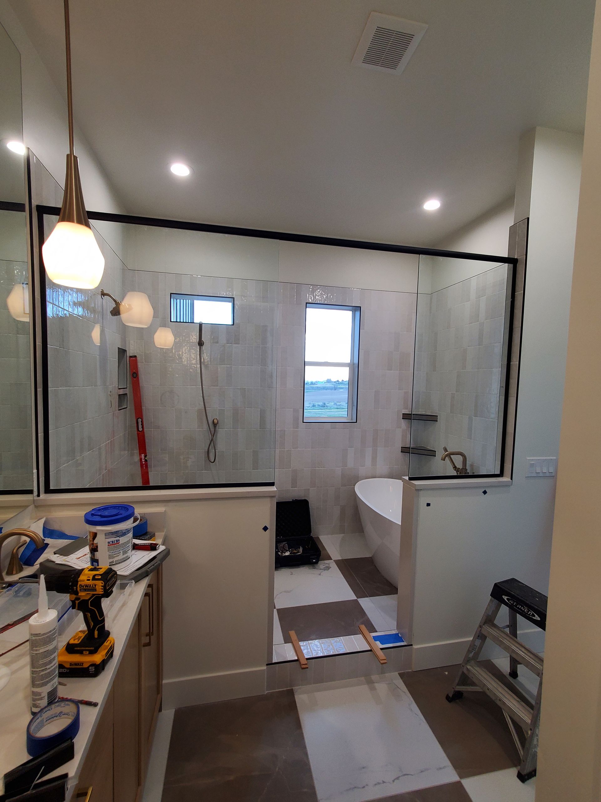 Bathroom under renovation with glass shower partition, exposed wall, and tools on the floor.