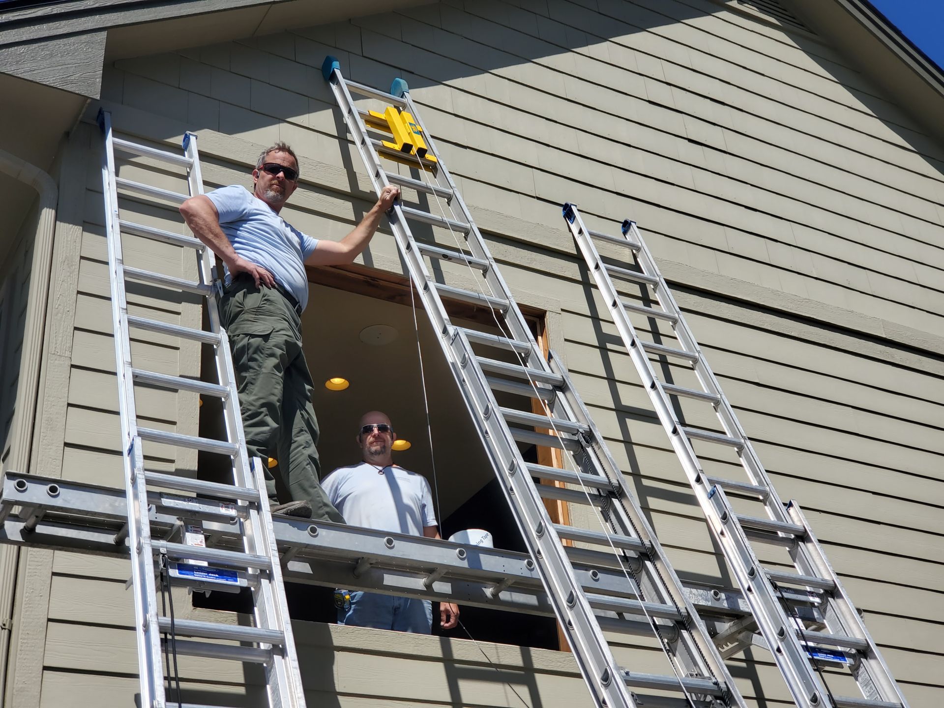 Two workers on ladders repairing a house exterior under the eaves