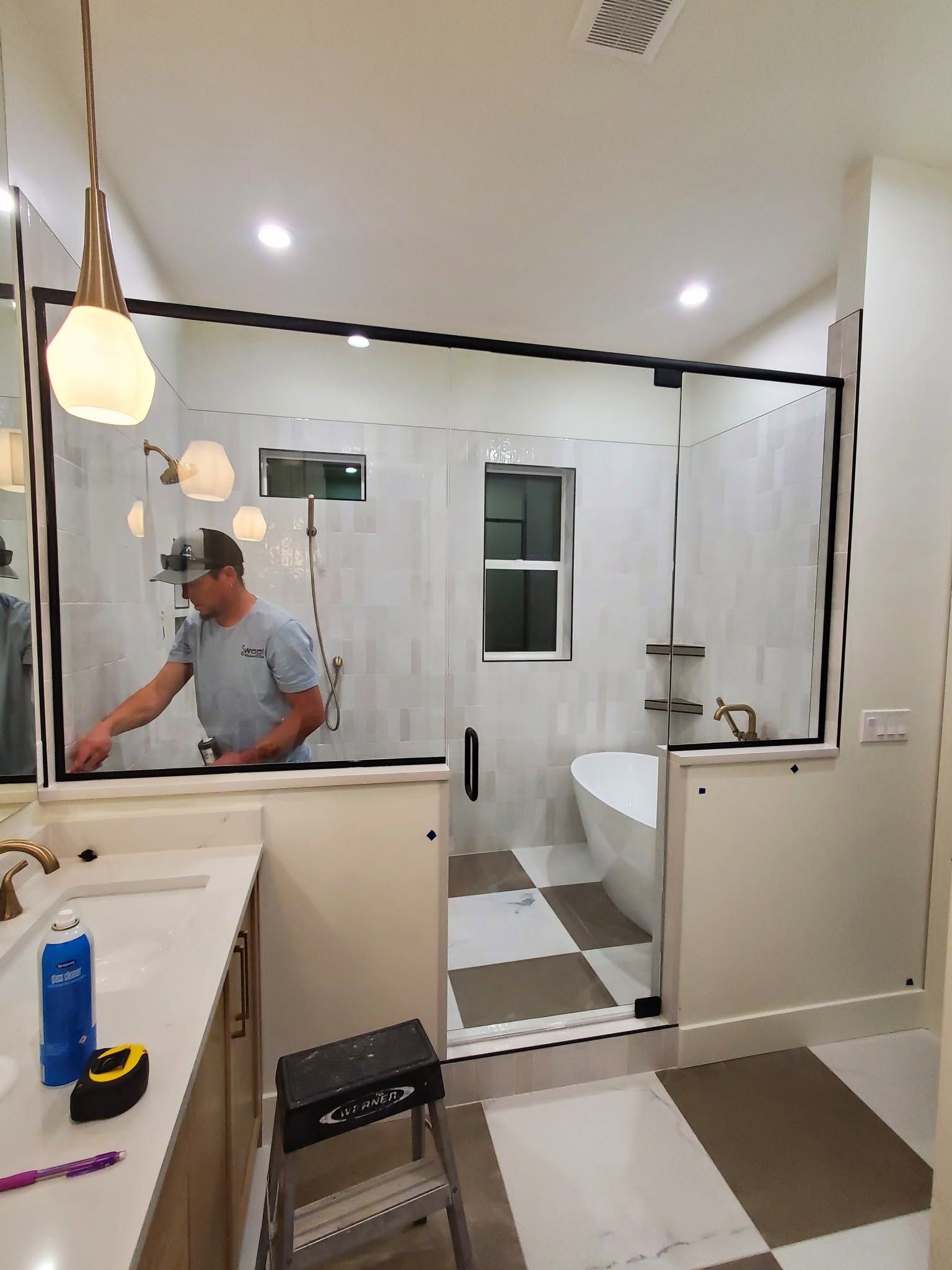 Bathroom under renovation with a worker cleaning near a sink and a shower in the background.