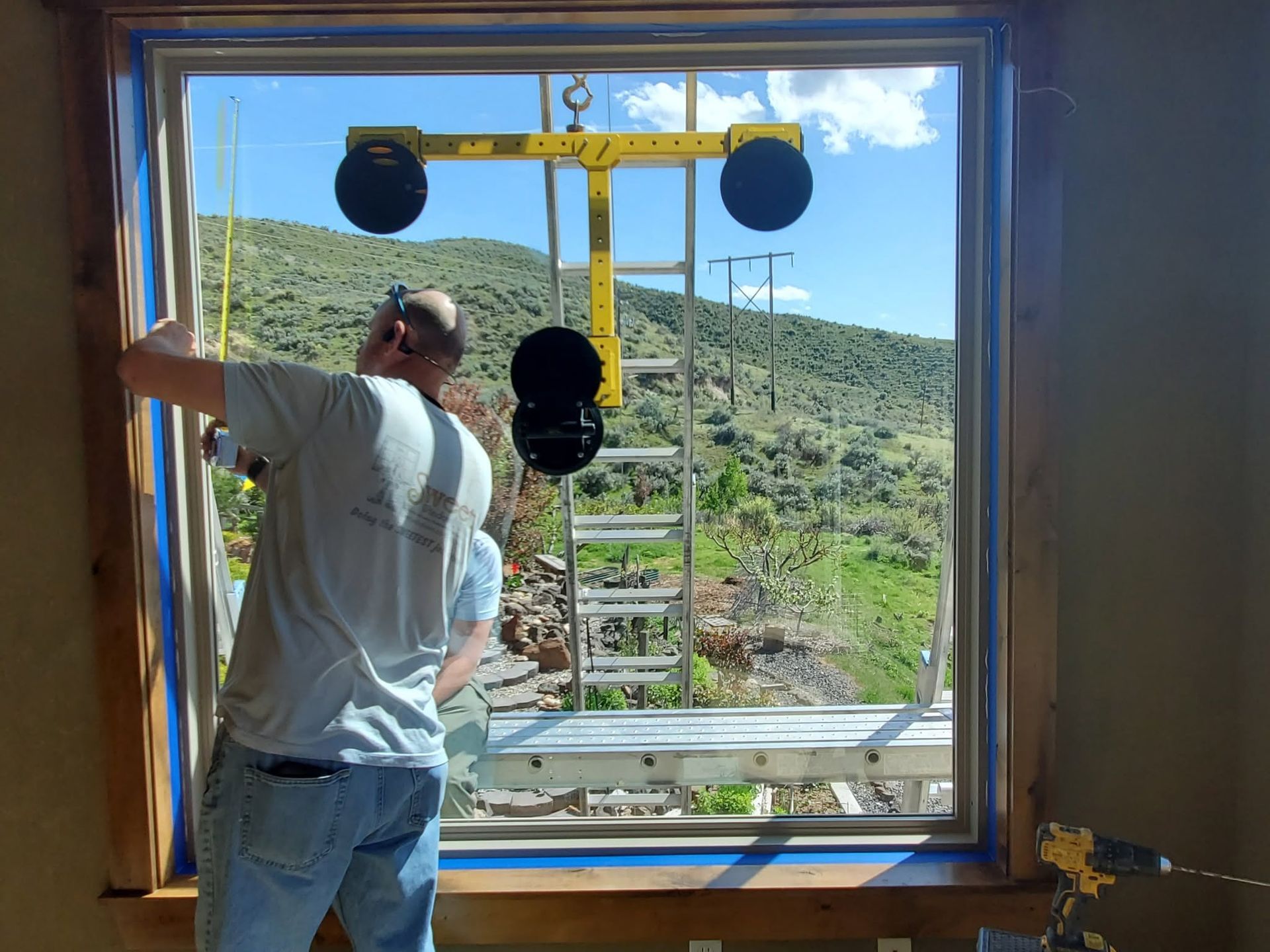 Worker installing a window frame indoors, with mountains and blue sky visible outside.