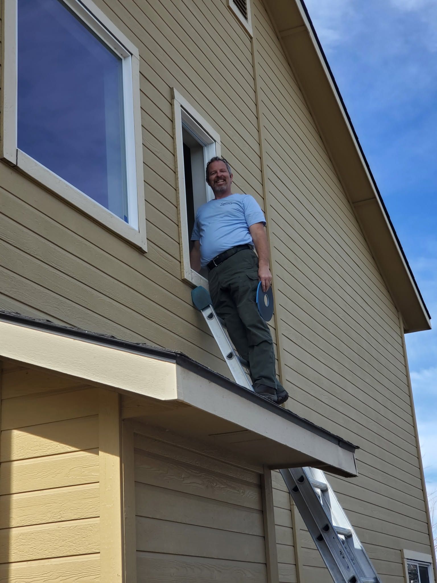 Person standing on a roof edge beside a ladder, near a doorway on a tan house