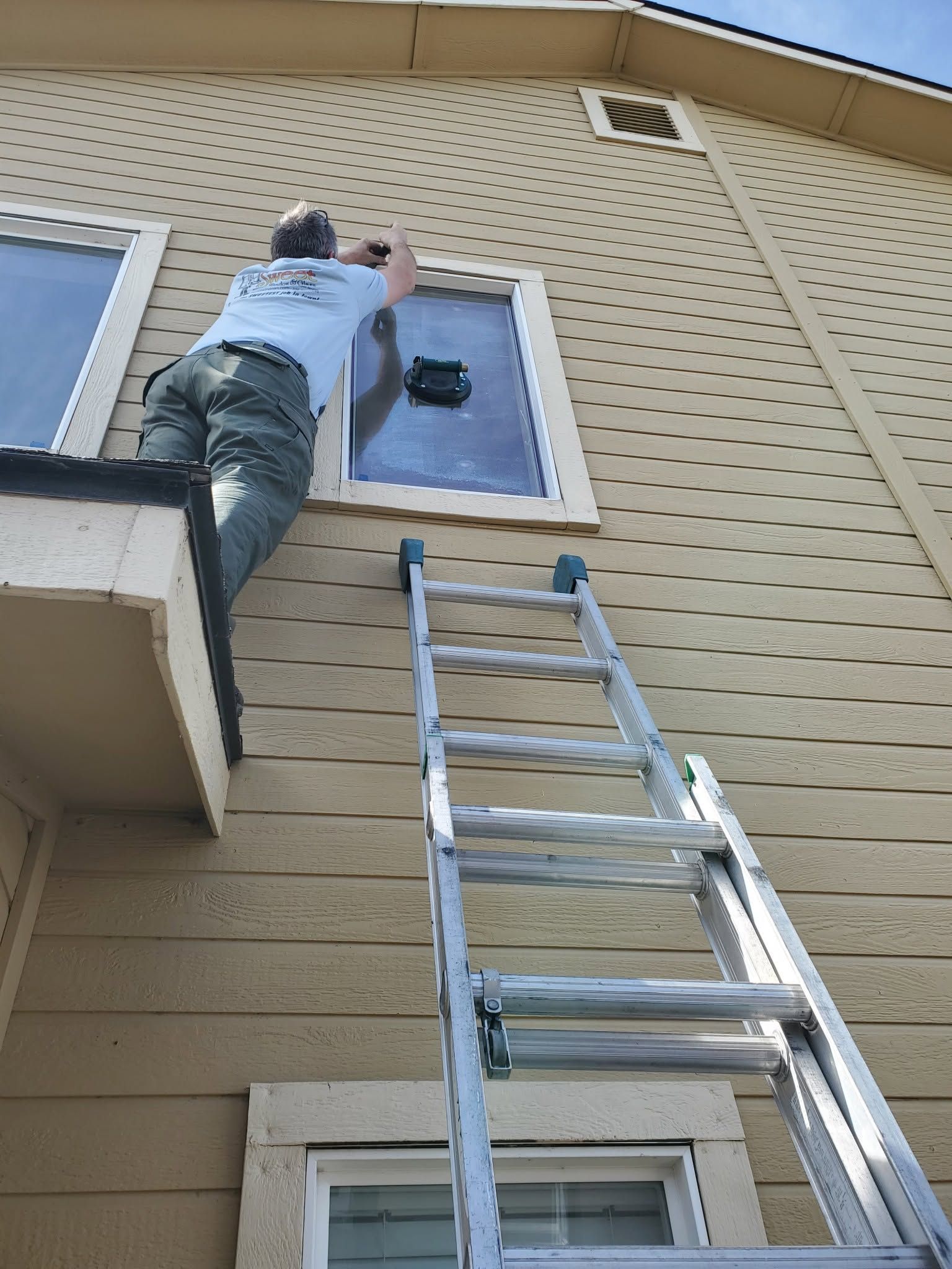 Person on a ladder reaching toward an upstairs window on a beige house