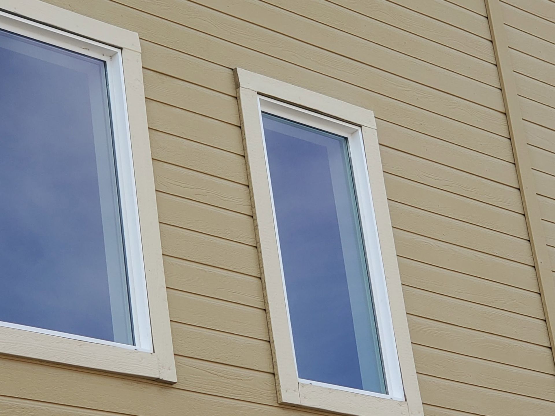 Two rectangular windows in a beige siding wall, one wide and one narrow.