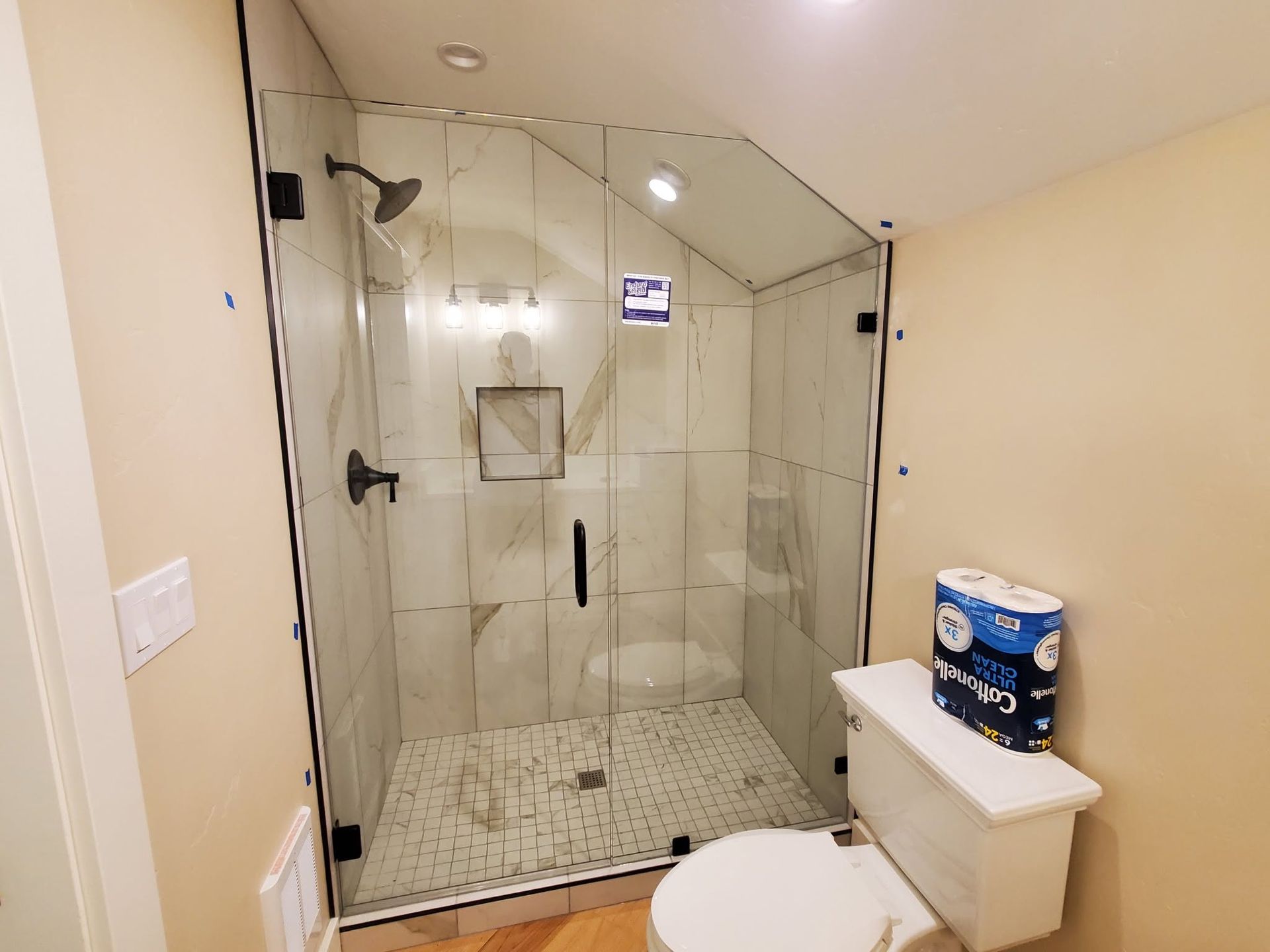 Bathroom with glass walk-in shower, beige walls, and toilet paper on the toilet tank.