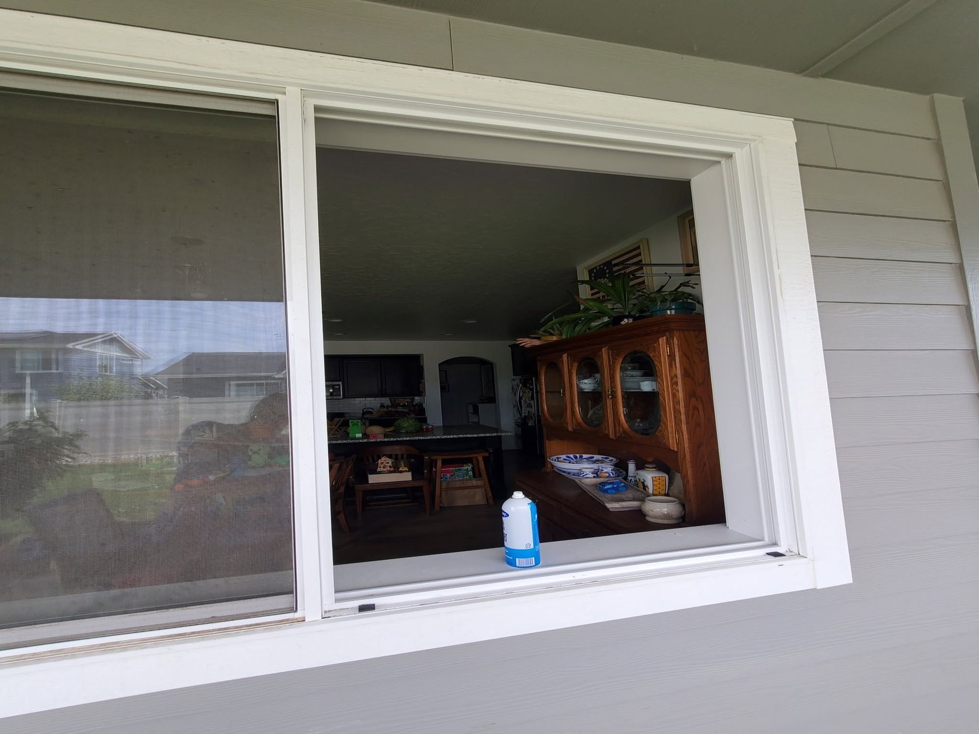 Open window with screen, showing a living room and wooden cabinet inside.