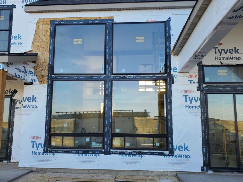 New house exterior with four black-framed windows under construction over Tyvek house wrap