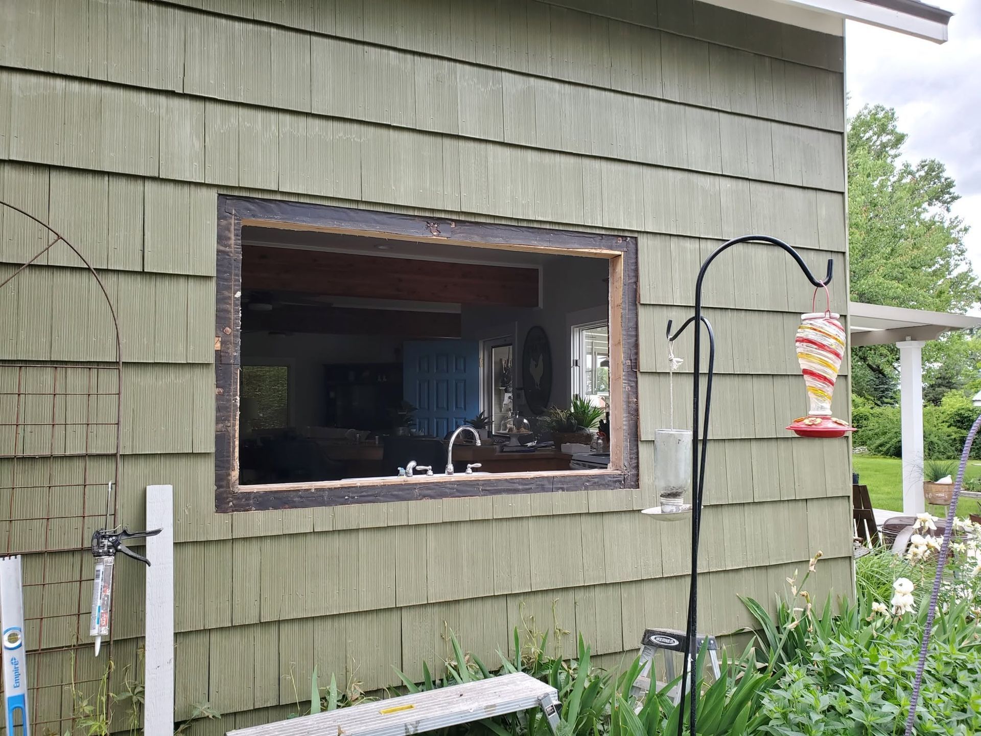 Open window in green house wall with garden plants and hanging bird feeder nearby