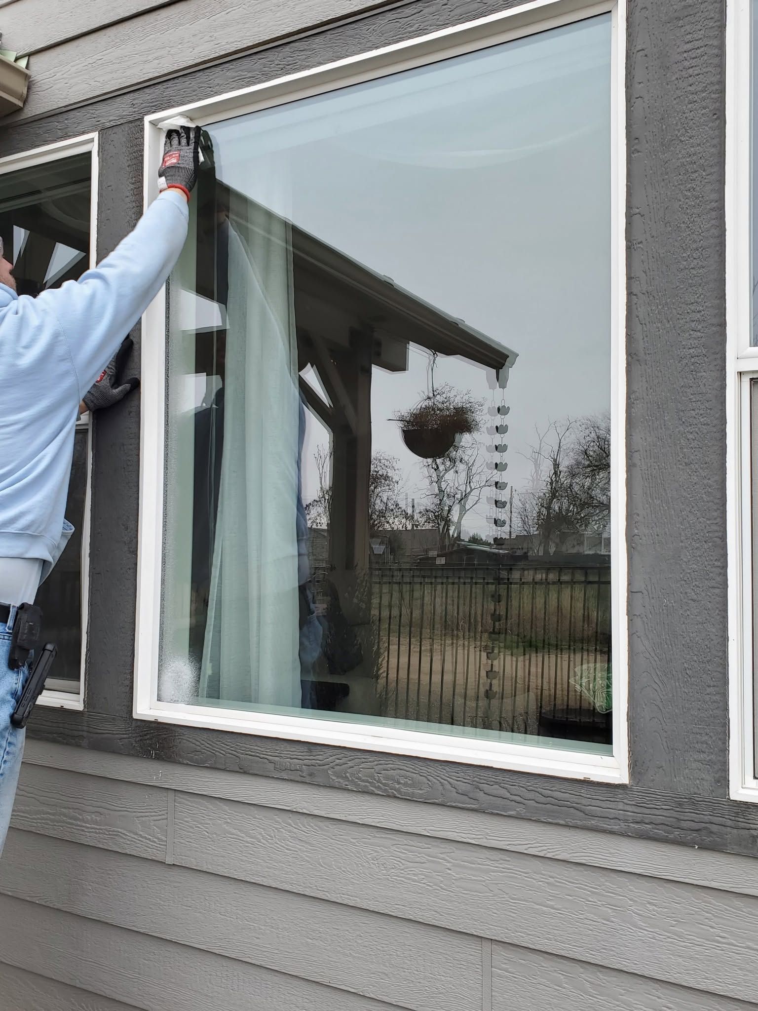 Worker cleaning a large exterior window beside gray siding