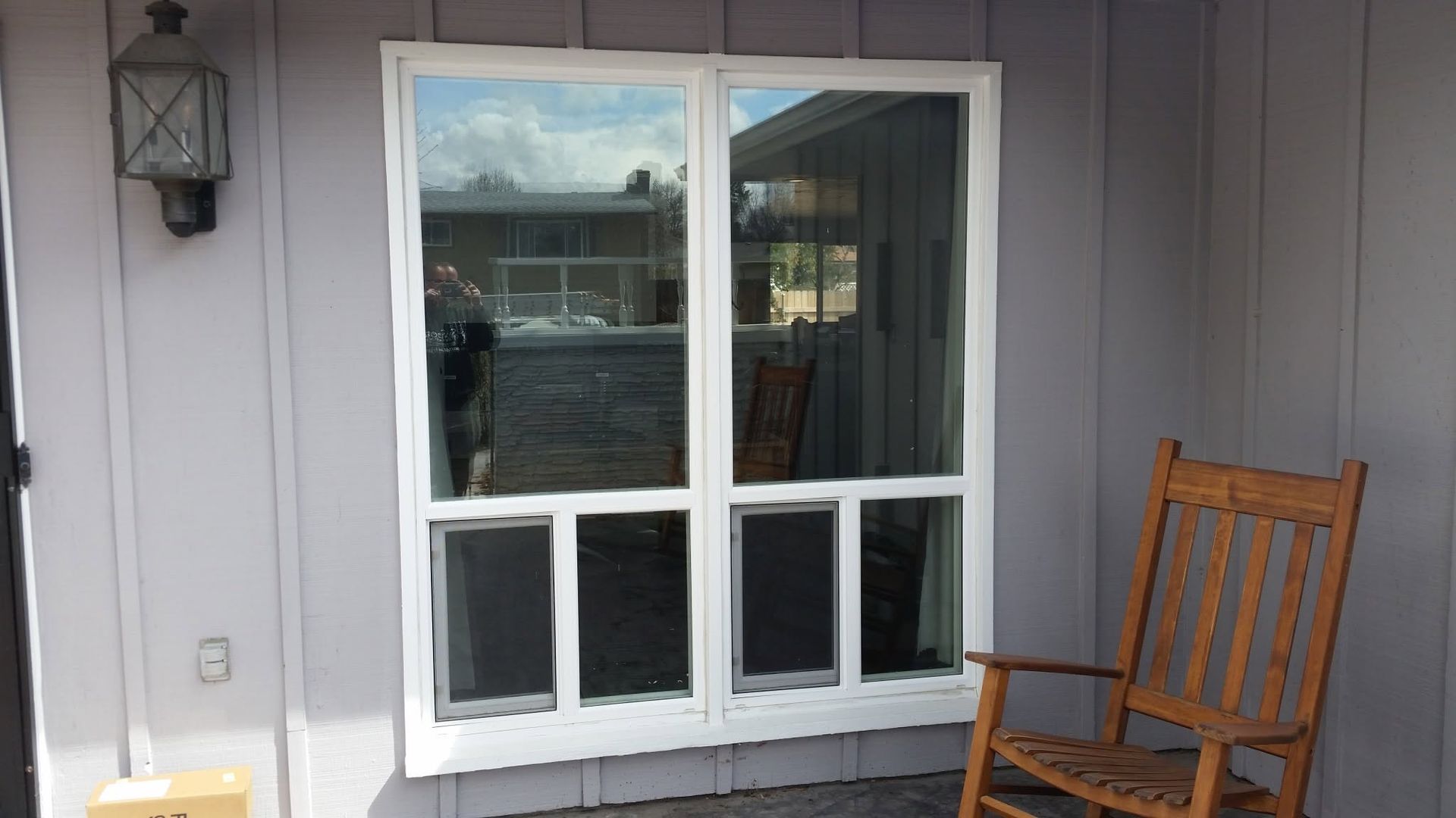 Front porch with a white-framed glass door, gray siding, and a wooden chair beside it.