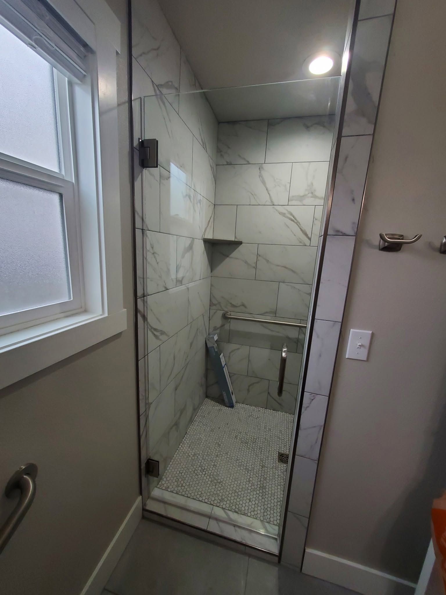 Small tiled shower stall with glass door beside a windowed bathroom wall