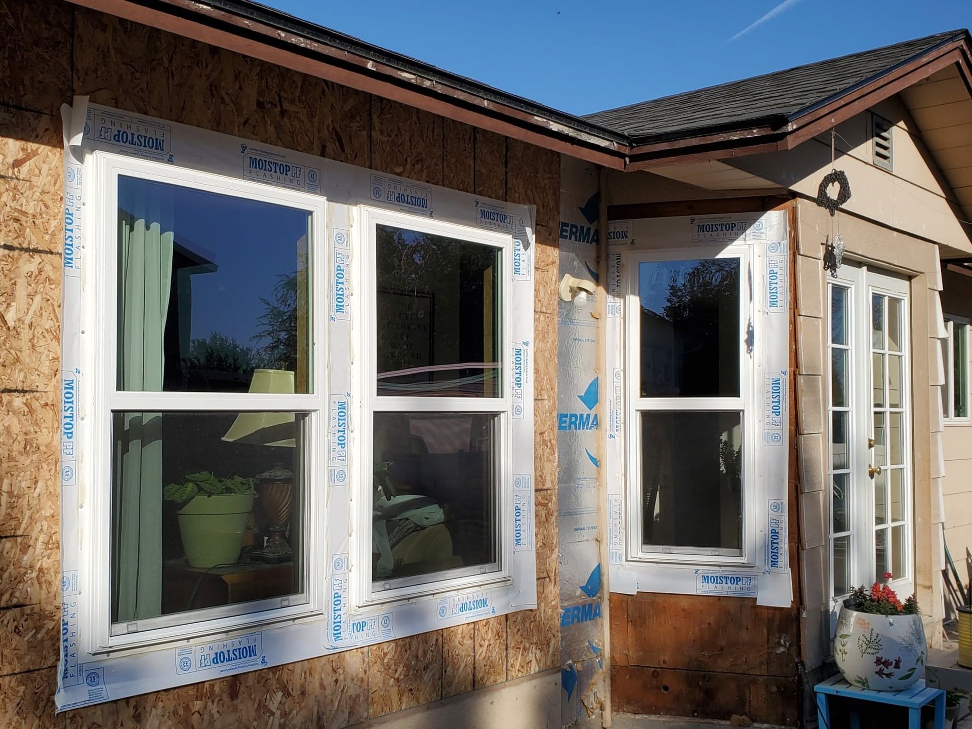 Exterior of a house with three white-framed windows and blue protective wrap around the trim