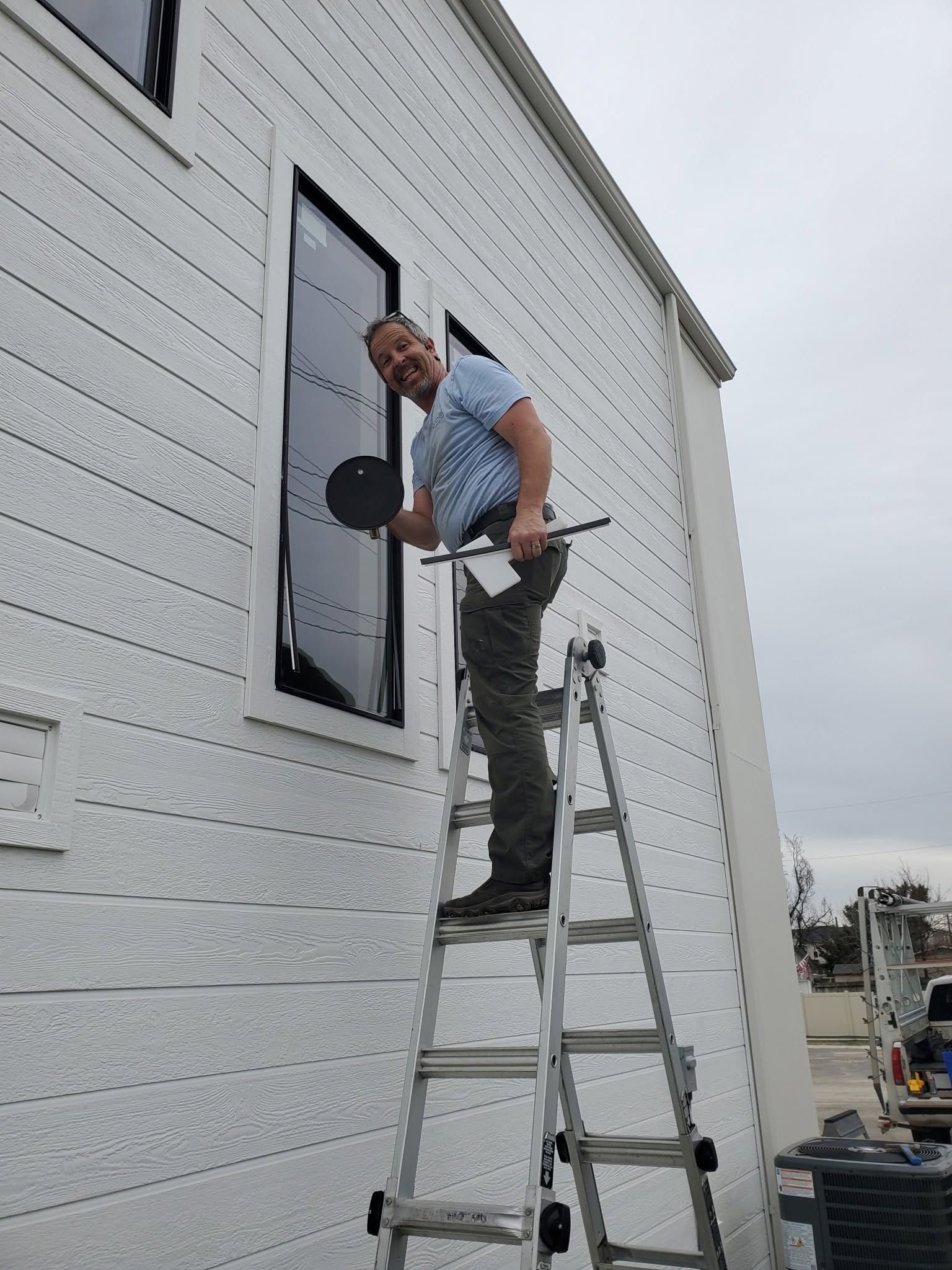 Worker on a ladder painting a tall white building near a window.
